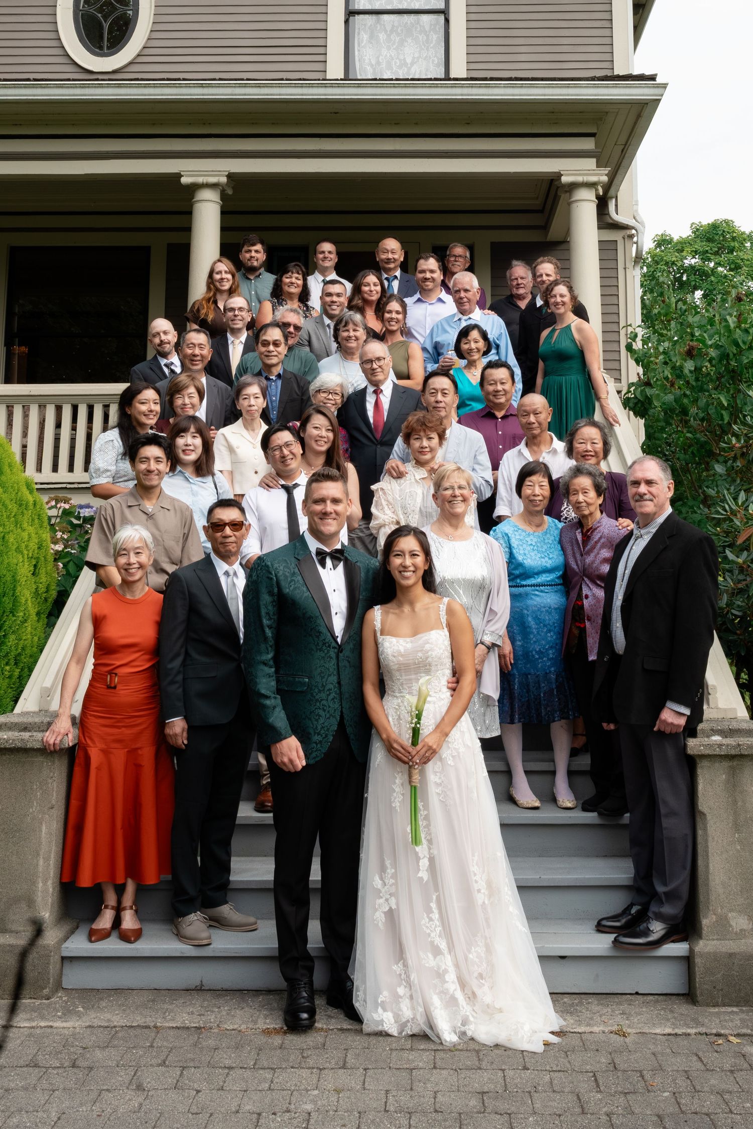 Large wedding group portrait on Victorian house steps with bride and groom in front.