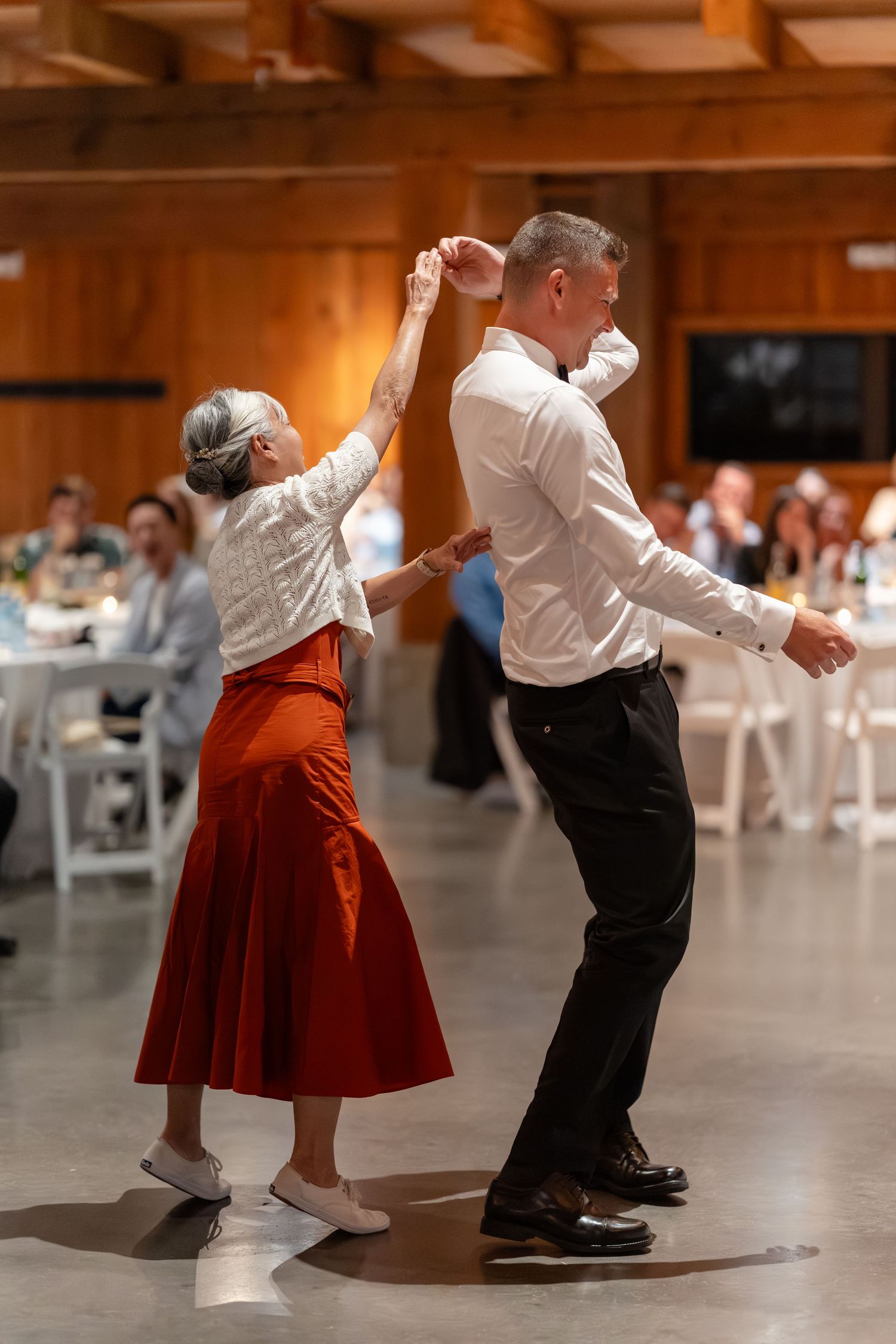 Older couple dancing energetically at wedding reception in rustic barn venue.