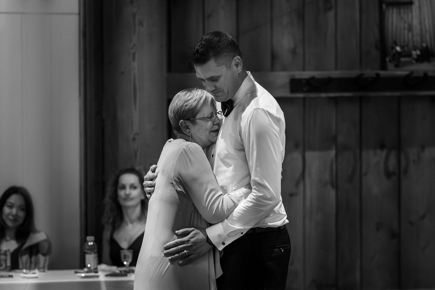 Groom shares tender mother-son dance at wedding reception in black and white.