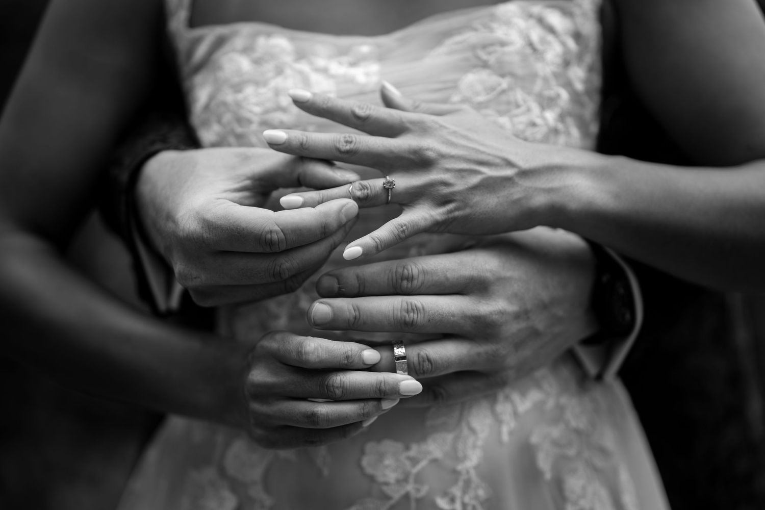 Black and white close-up of bride and groom intertwining hands showing wedding rings.
