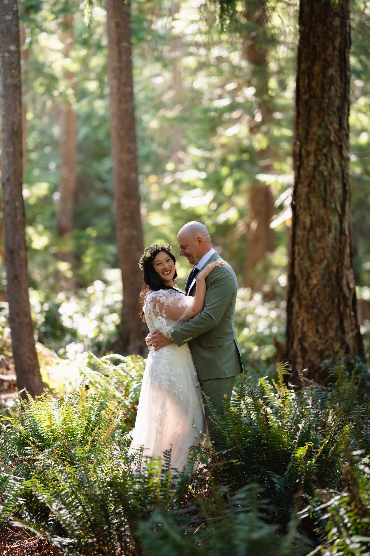 A bride and groom embrace romantically in a sunlit forest during their wedding day.