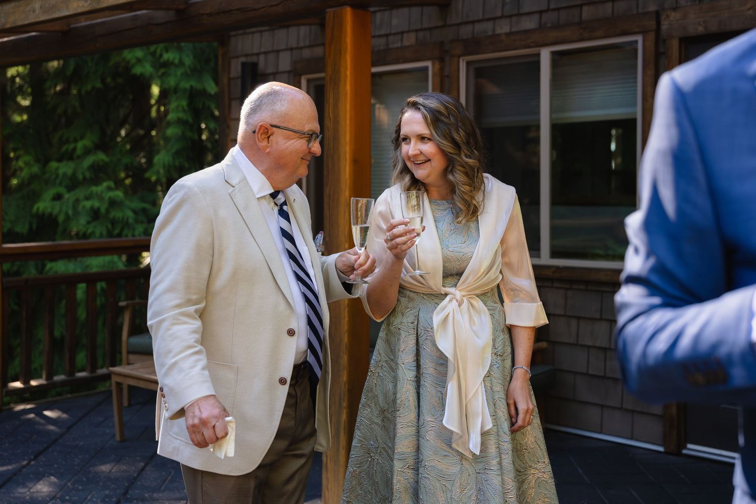 An elegantly dressed couple shares a cheerful conversation while holding champagne glasses at a wedding reception.