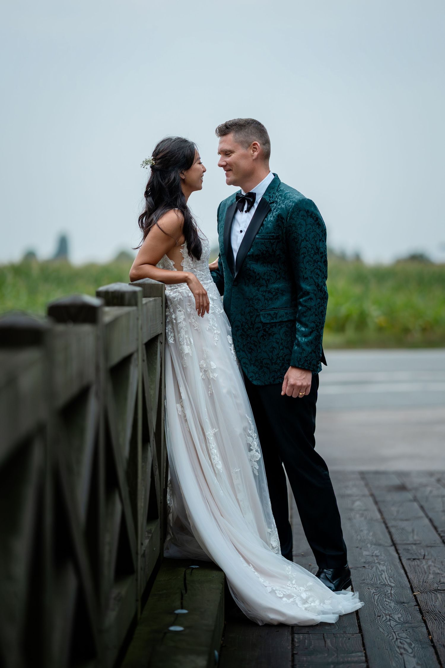 Bride and groom share intimate moment on wooden bridge at waterfront.