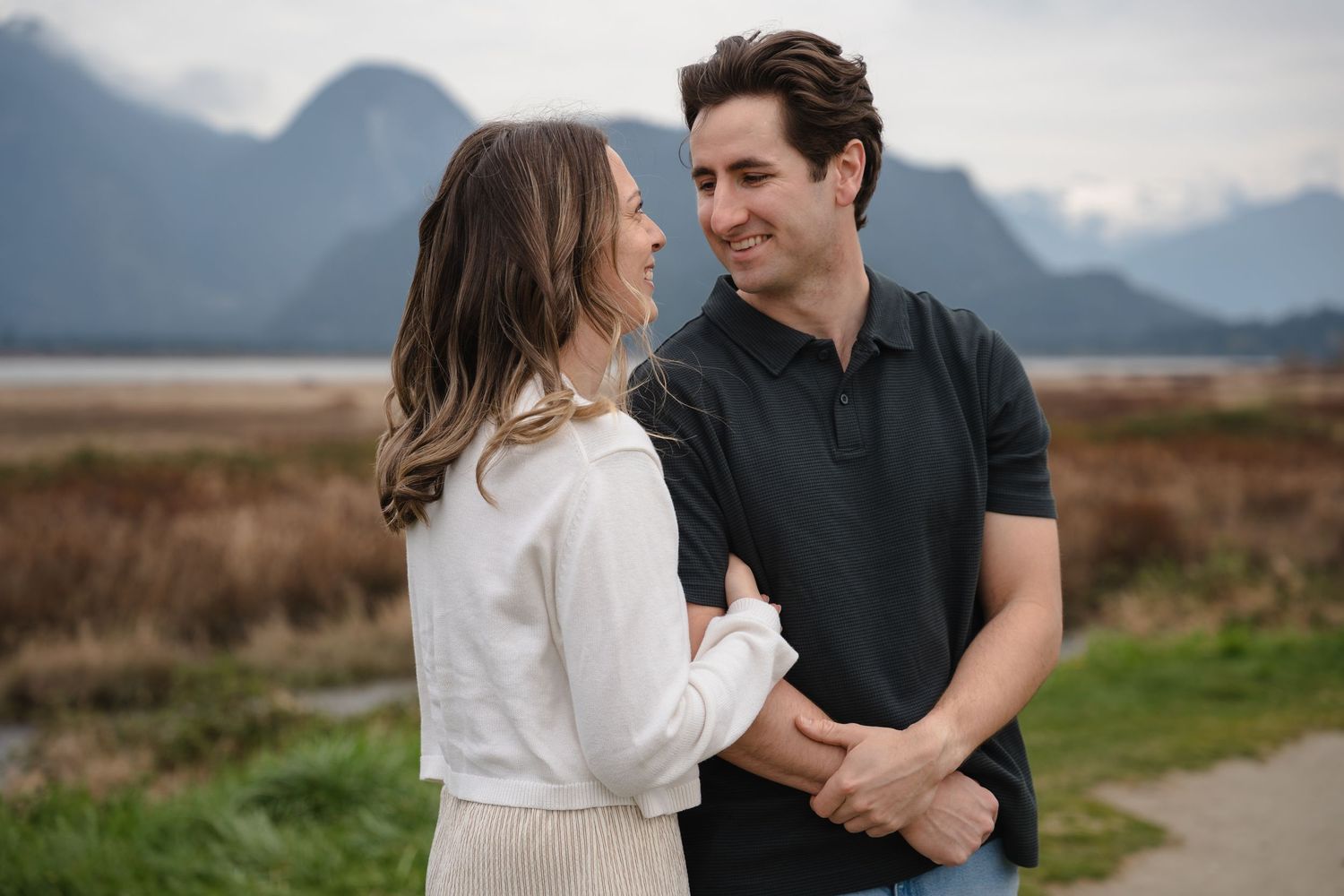 Couple smiling at each other outdoors with mountains and a scenic landscape in the background.