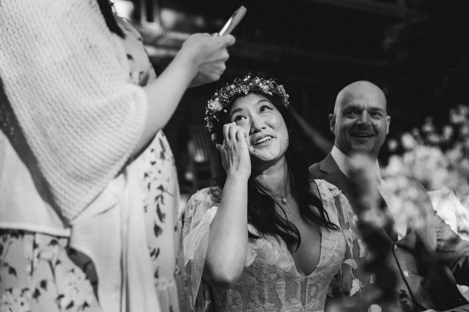 Emotional bride in floral crown wiping tears during outdoor wedding ceremony in black and white.