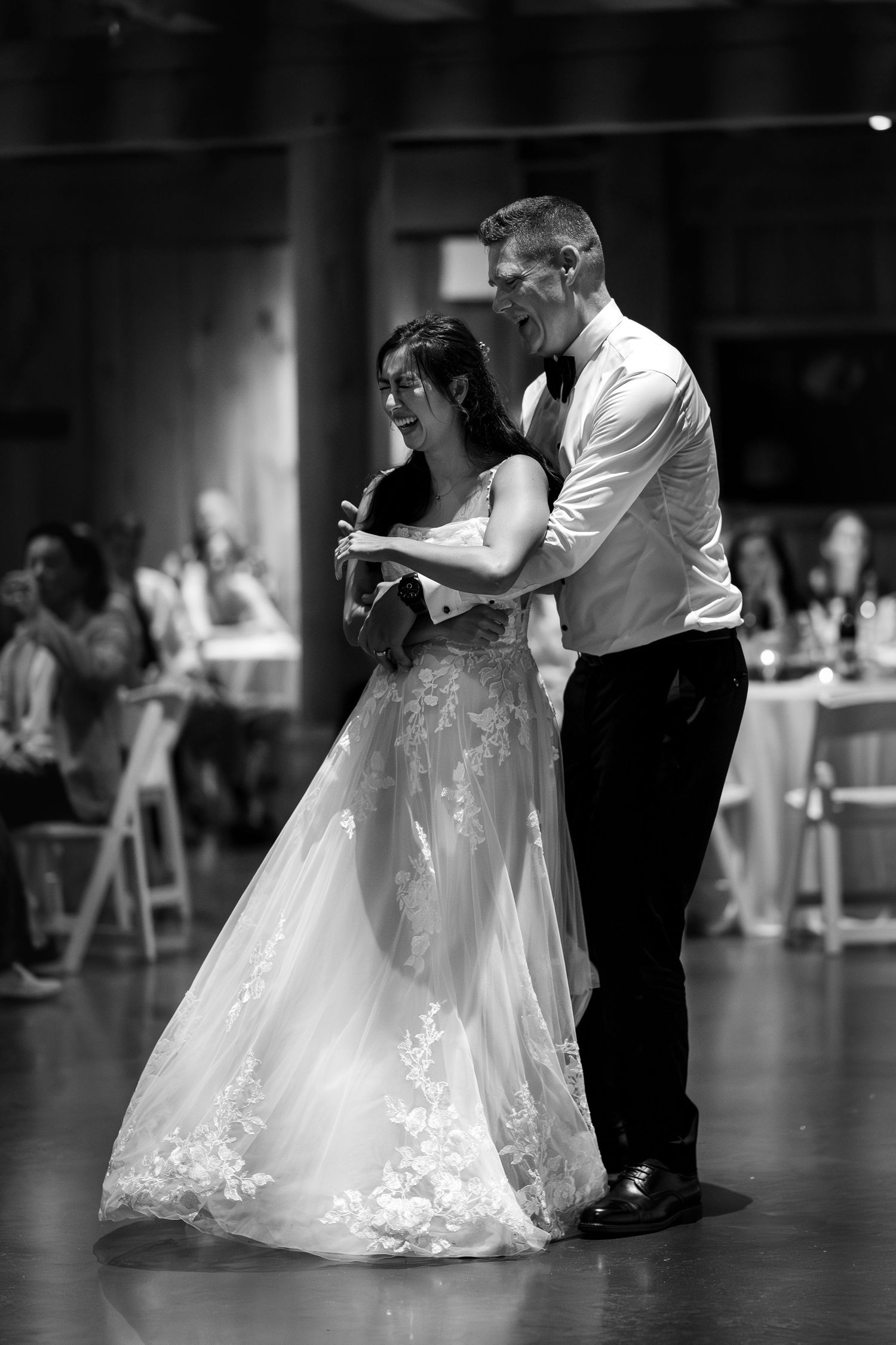 Bride and groom share joyful first dance in black and white photo.