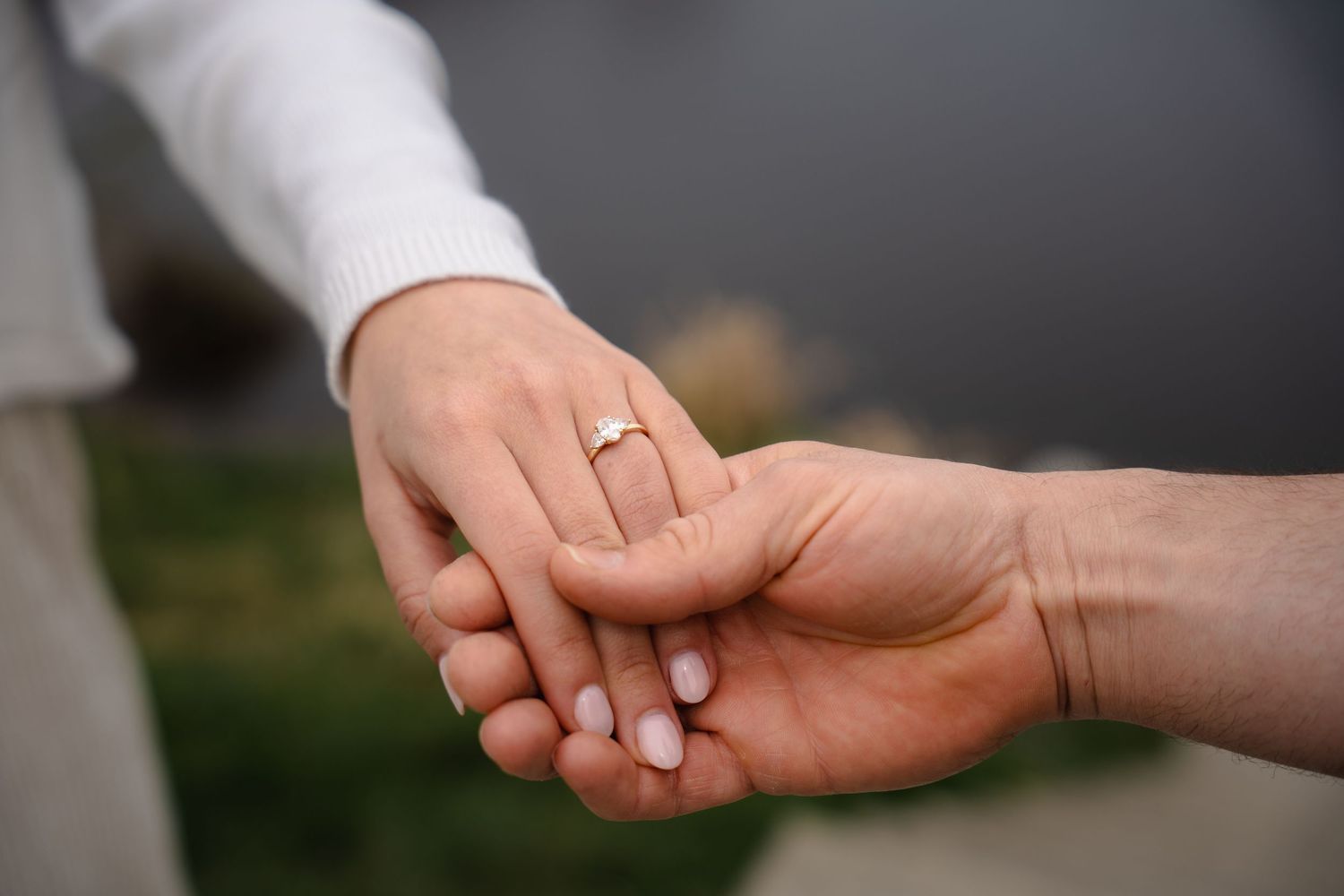 Close-up of two hands held together, one wearing a gold diamond engagement ring, symbolizing love and commitment.