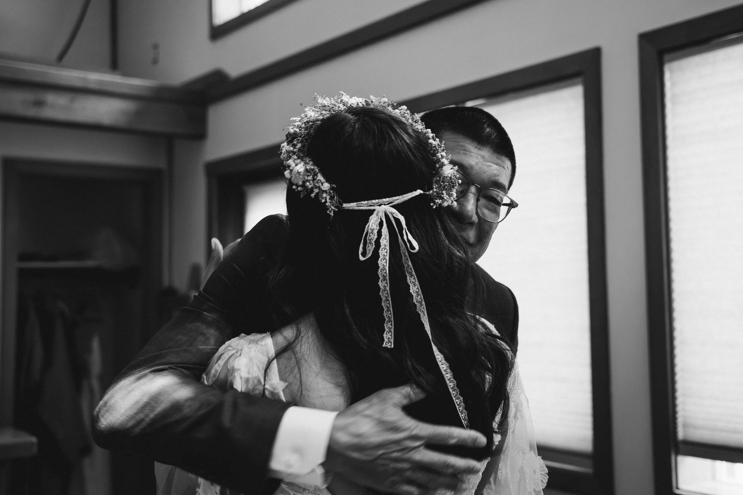 Emotional black and white photo of a groom hugging bride wearing a floral crown at a wedding.