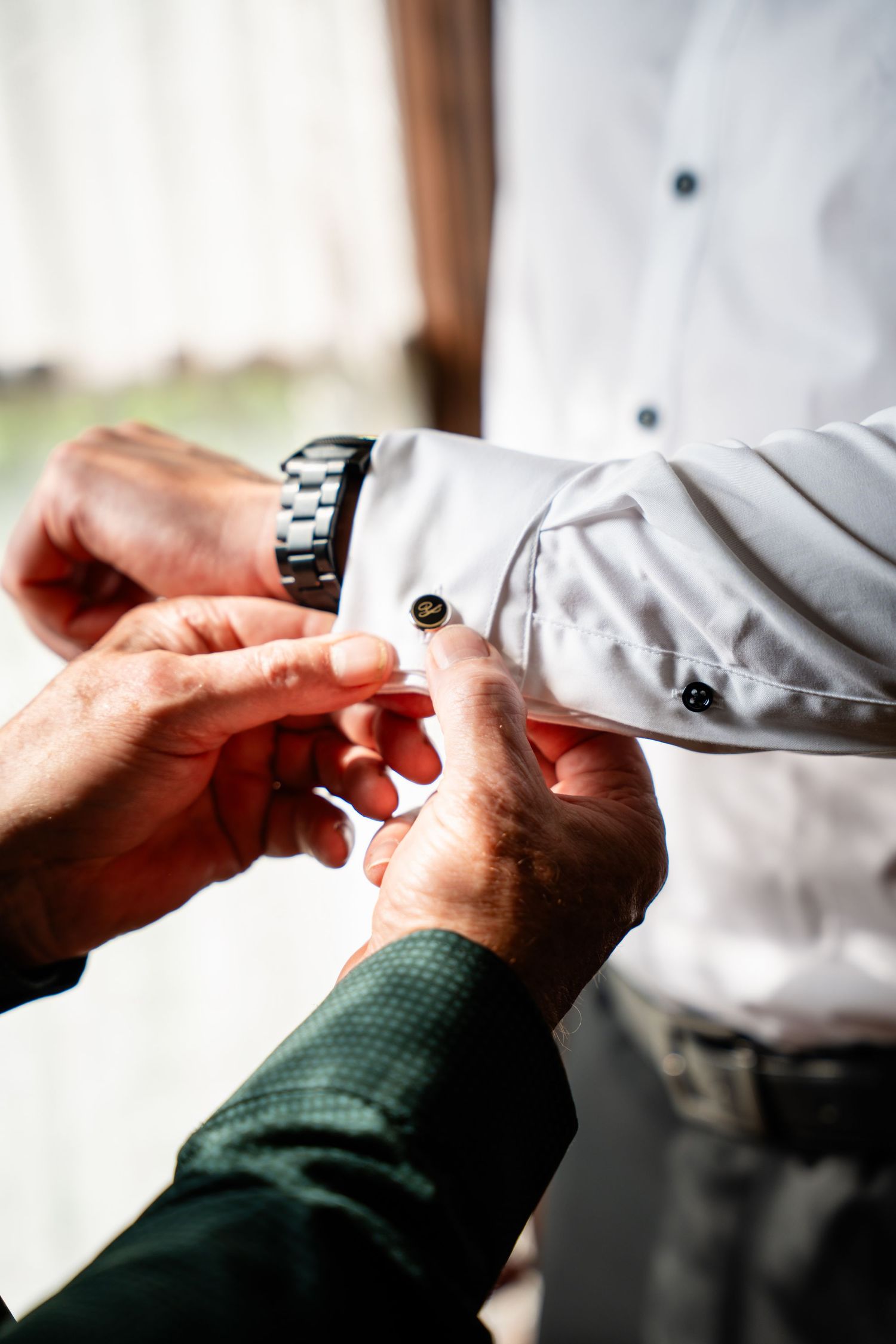 Close-up of hands fastening cufflink on groom's white dress shirt before wedding ceremony.