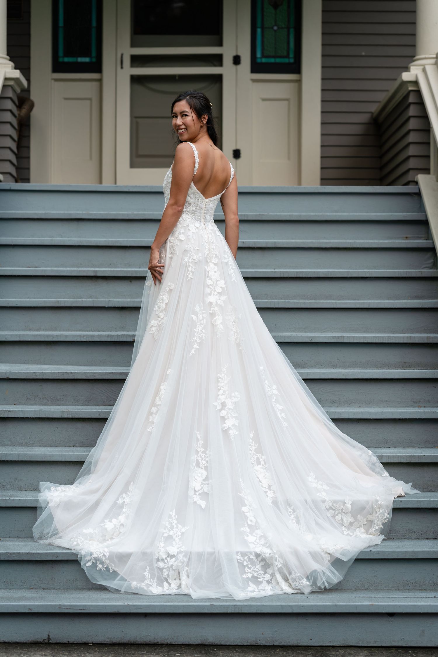 Bride in elegant lace A-line wedding gown with train on gray steps.