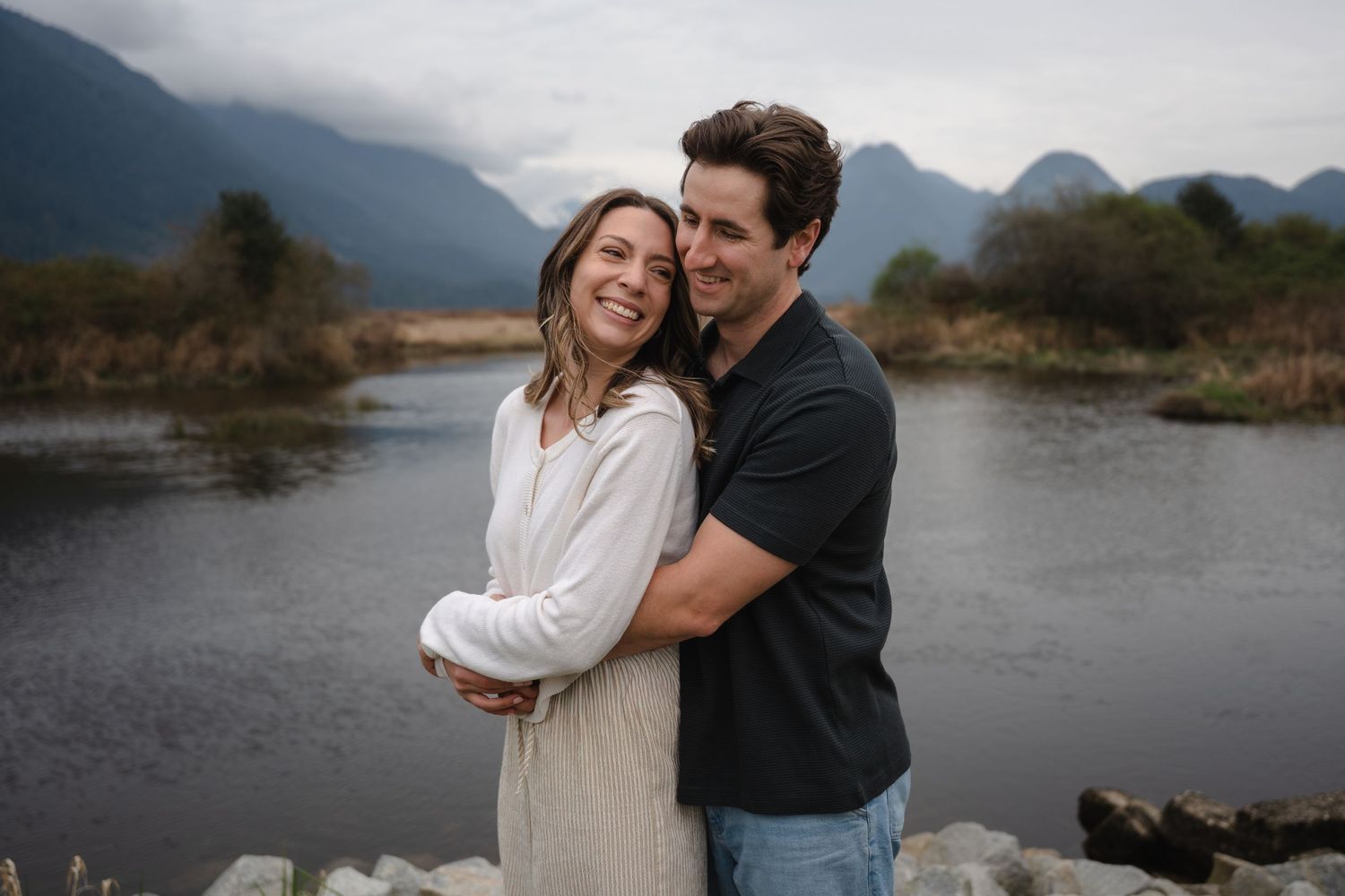Happy couple embracing outdoors near a river with misty mountains in the background.