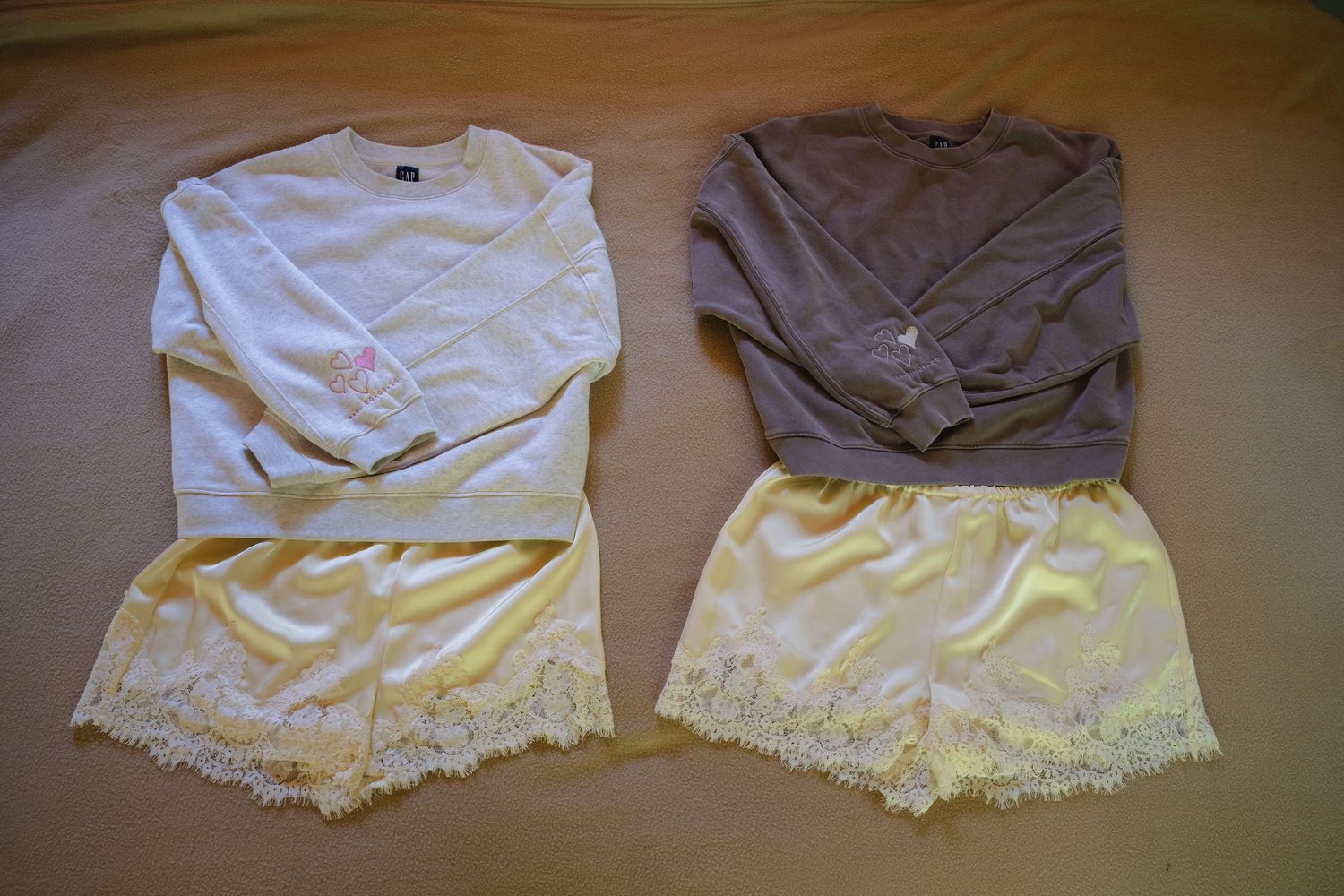 Two matching outfit sets with white and gray sweatshirts paired with yellow lace trim shorts laid flat on a beige surface.