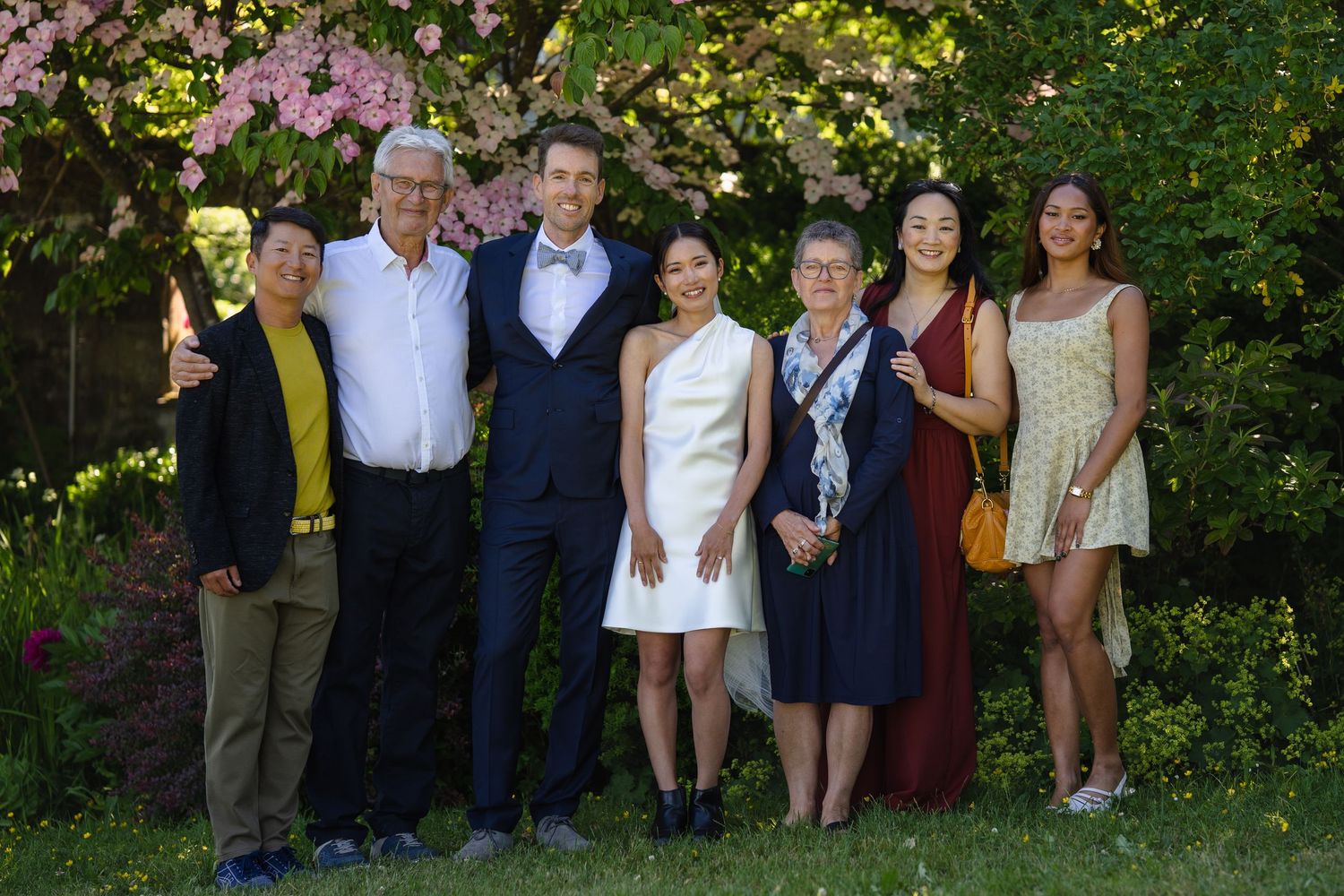 Group of seven people posing together outdoors in a garden during a formal celebration or wedding event.