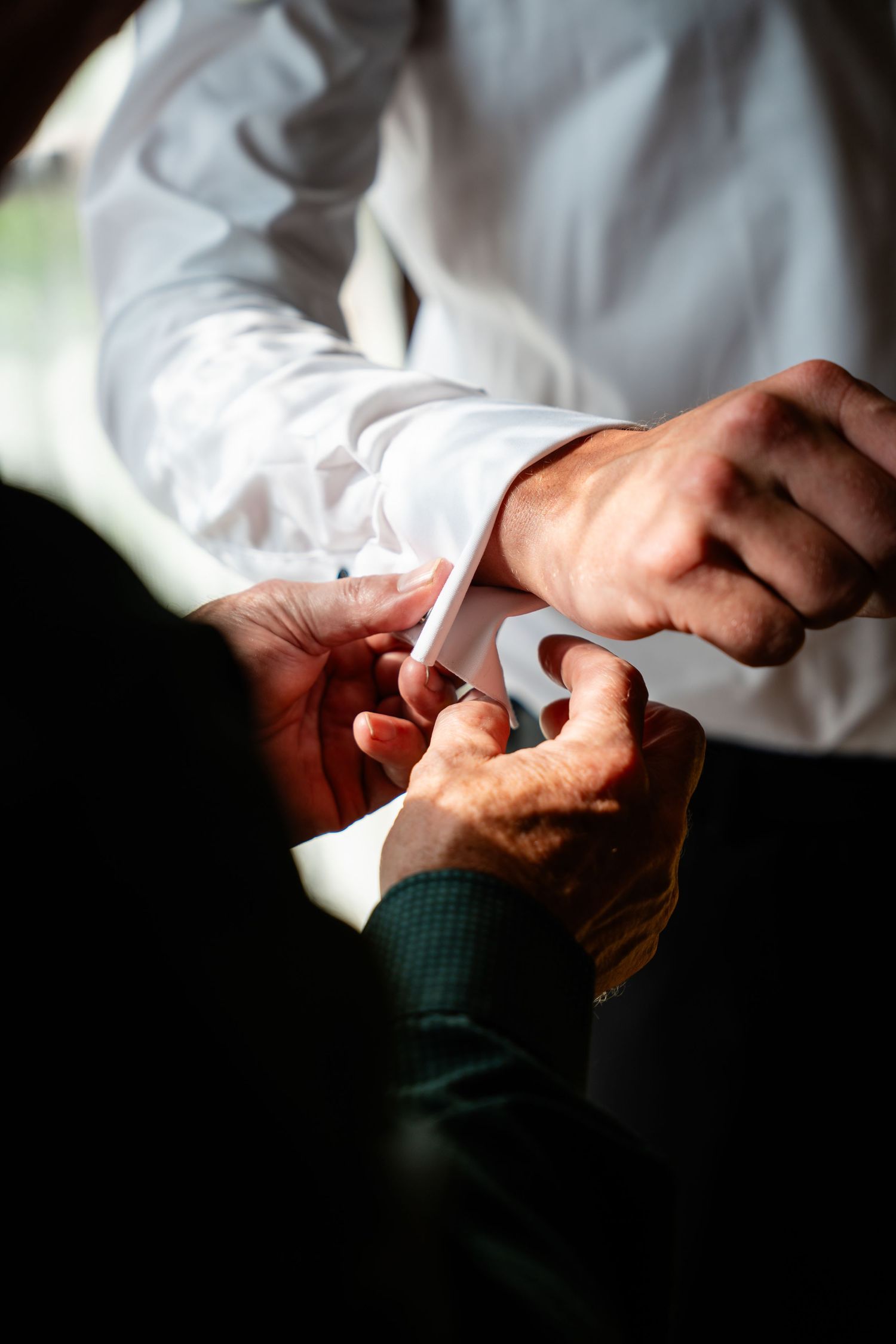 A man in a white dress shirt getting his cufflinks fastened by another person during wedding preparations.