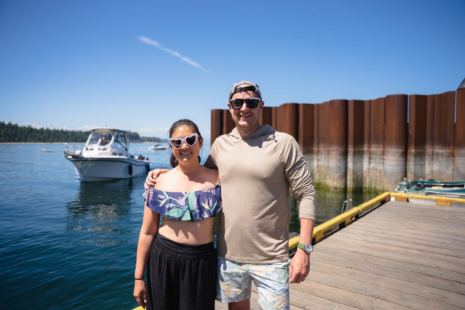 Couple posing on a sunny dock with a boat and blue lake in the background.