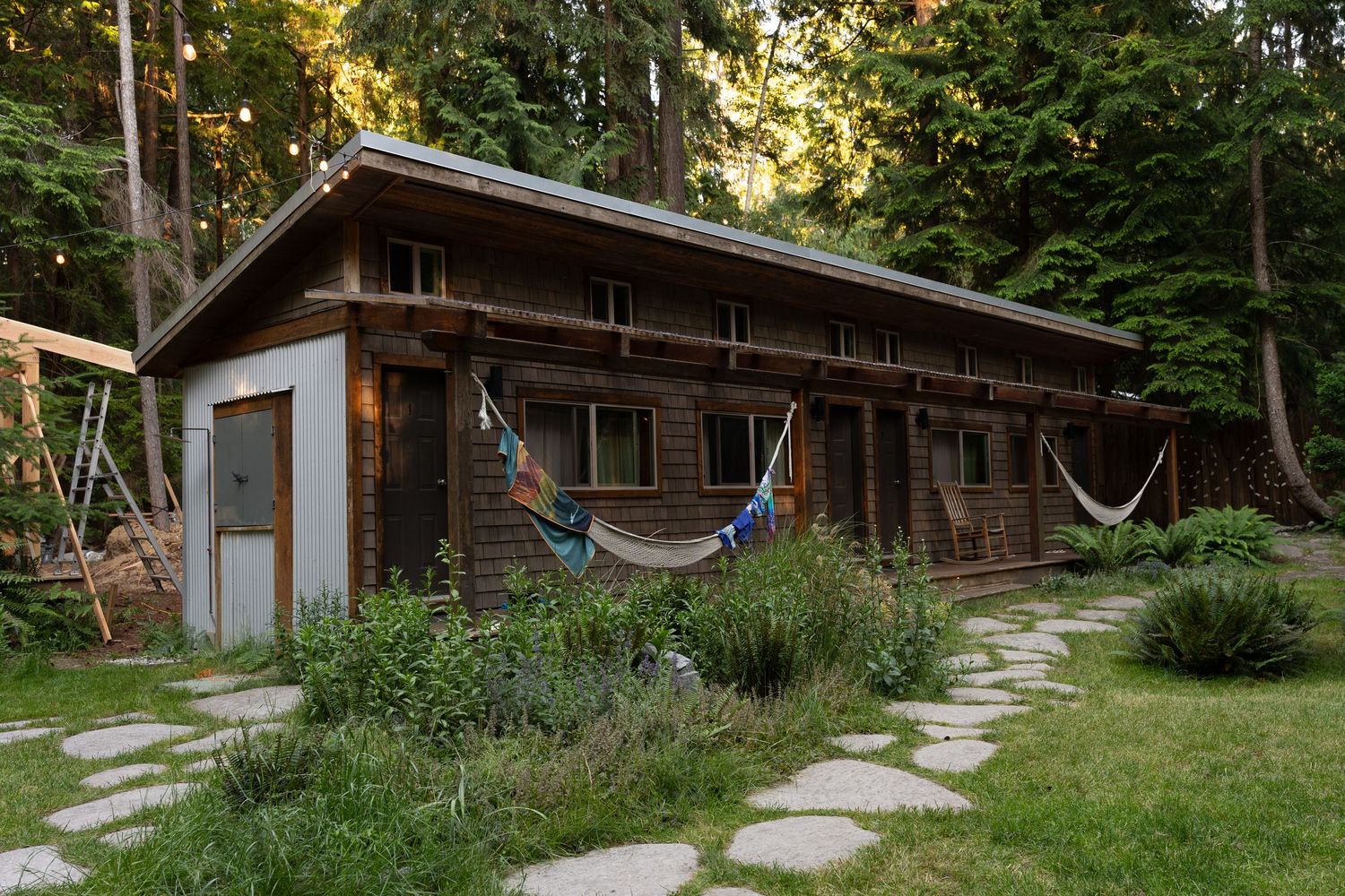 Rustic wooden cabin surrounded by tall trees with colorful hammocks in the yard.