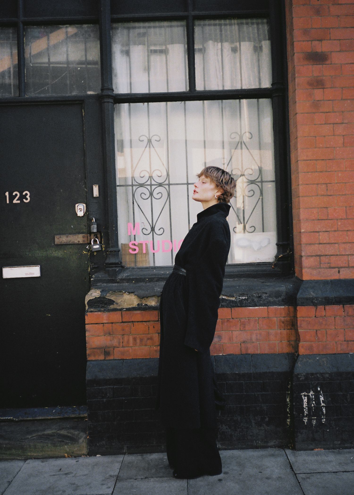A sequence of street photographs showing a person in black clothing walking past brick buildings with white window frames.