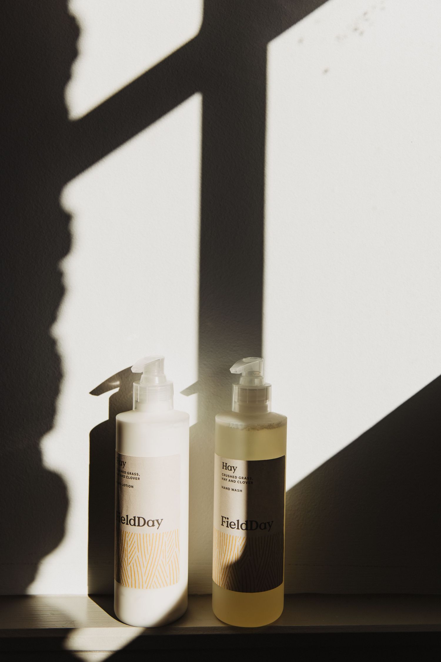Minimalist beauty product bottles casting dramatic diagonal shadows against a white wall in natural light.