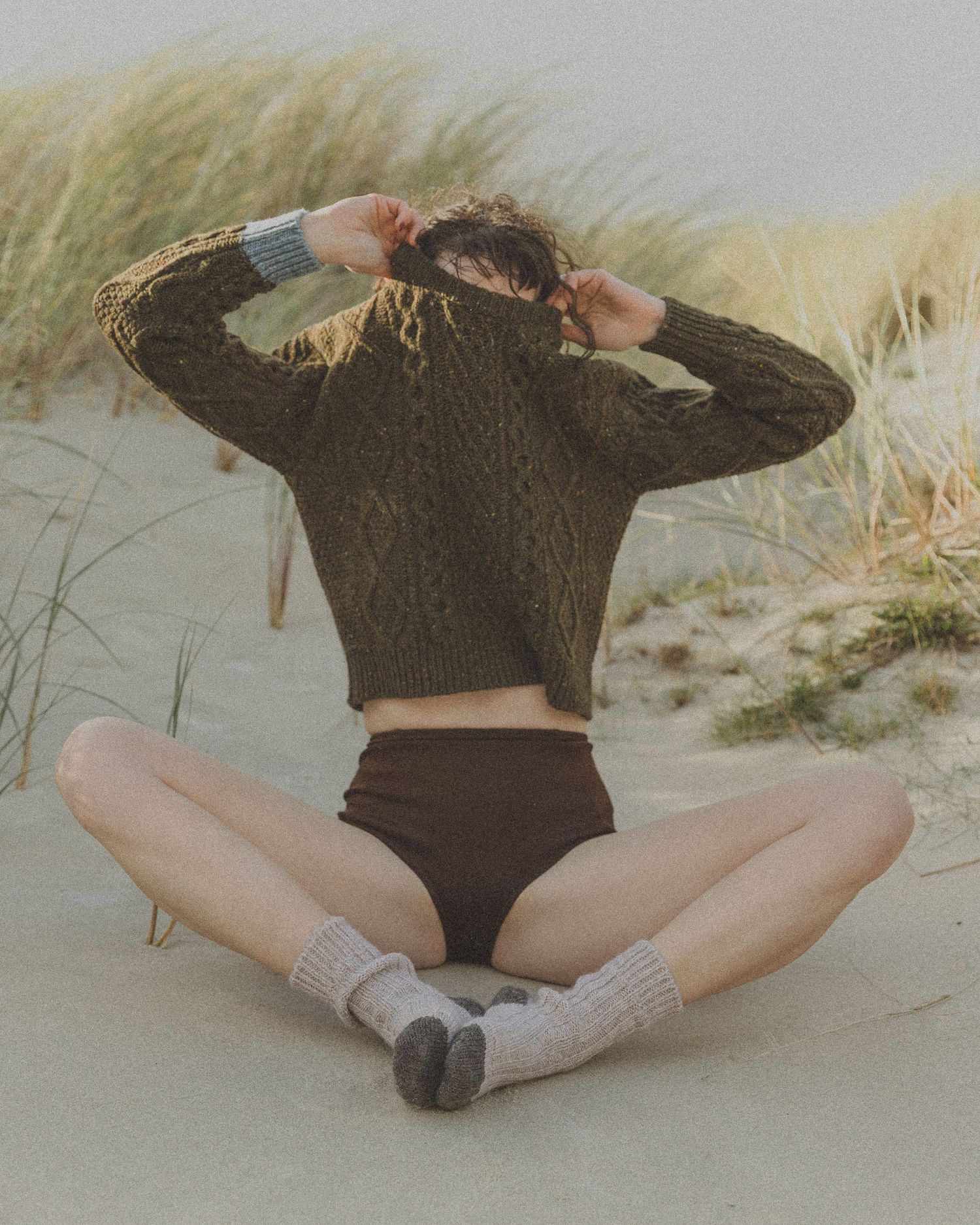 Artistic beach photos showing relaxed poses in dark sweater on sandy dunes.