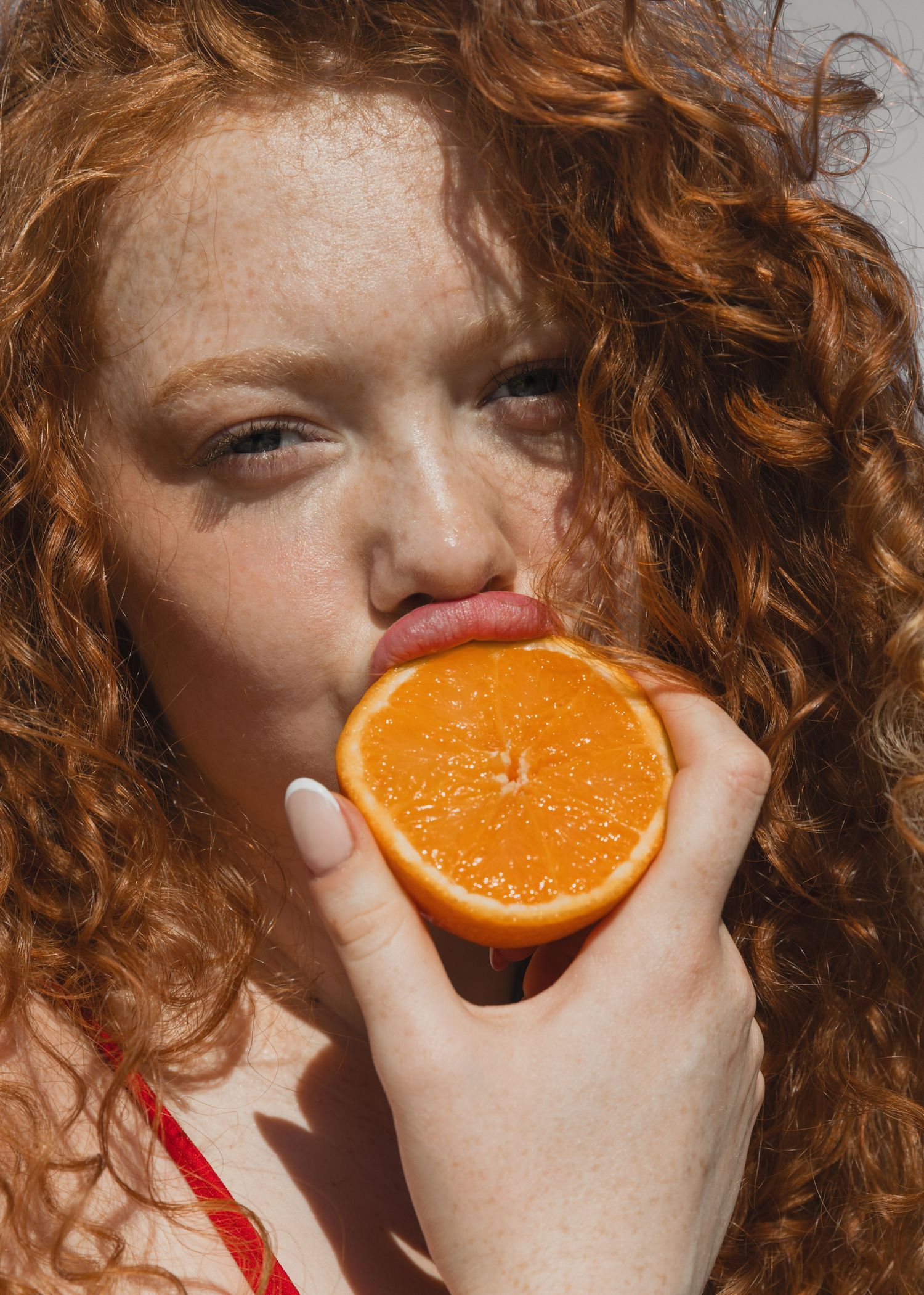 A sequence of photos showing a person with curly red hair taking bites from a fresh orange slice.