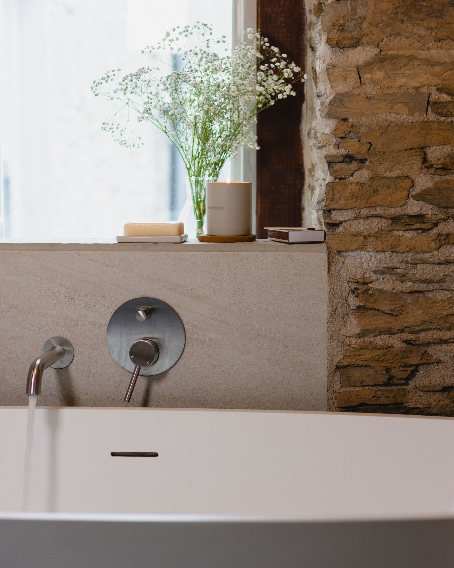 A rustic bathroom interior featuring a white bathtub against stone walls with small window ledges holding decorative items.