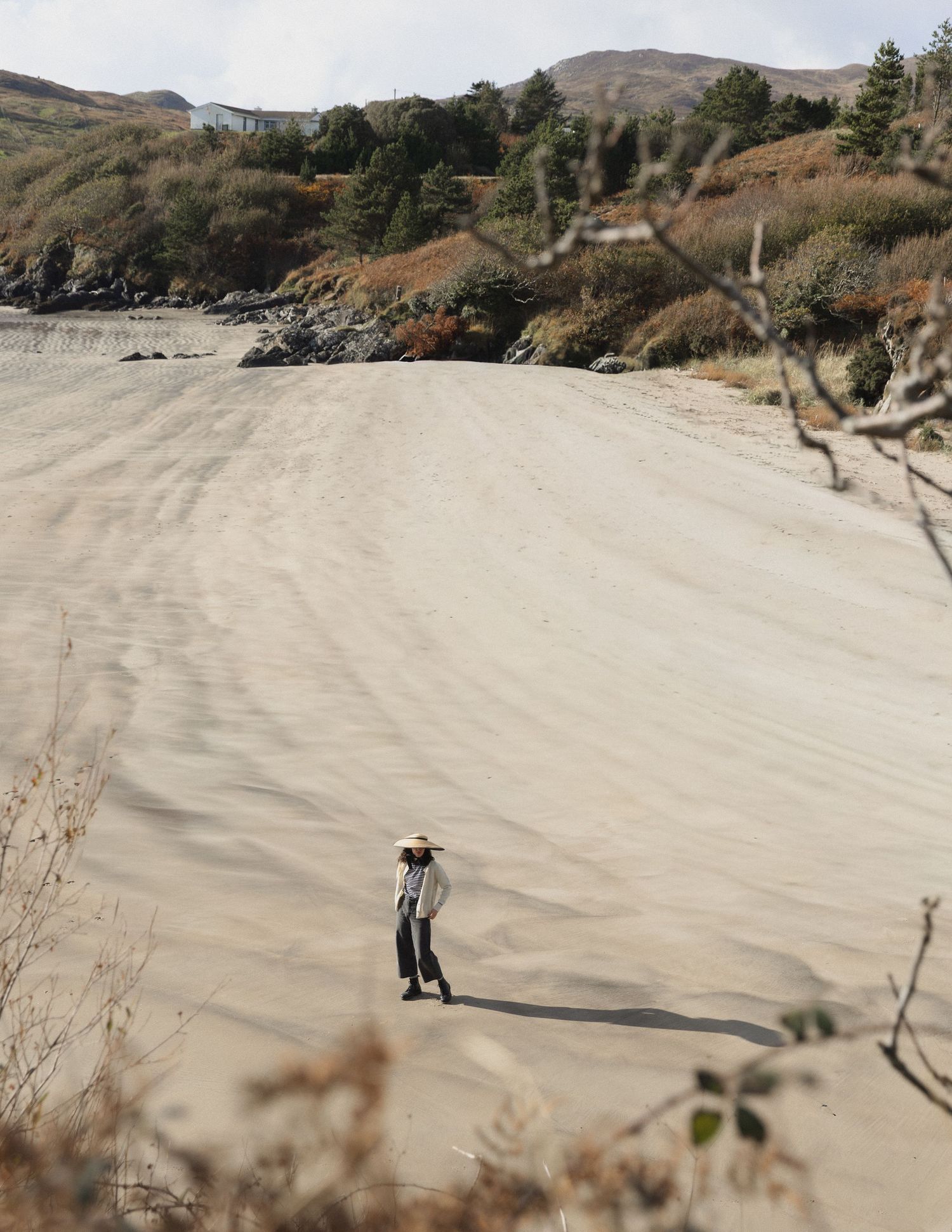 A figure stands on a vast sand dune against a mountainous backdrop in dramatic lighting.
