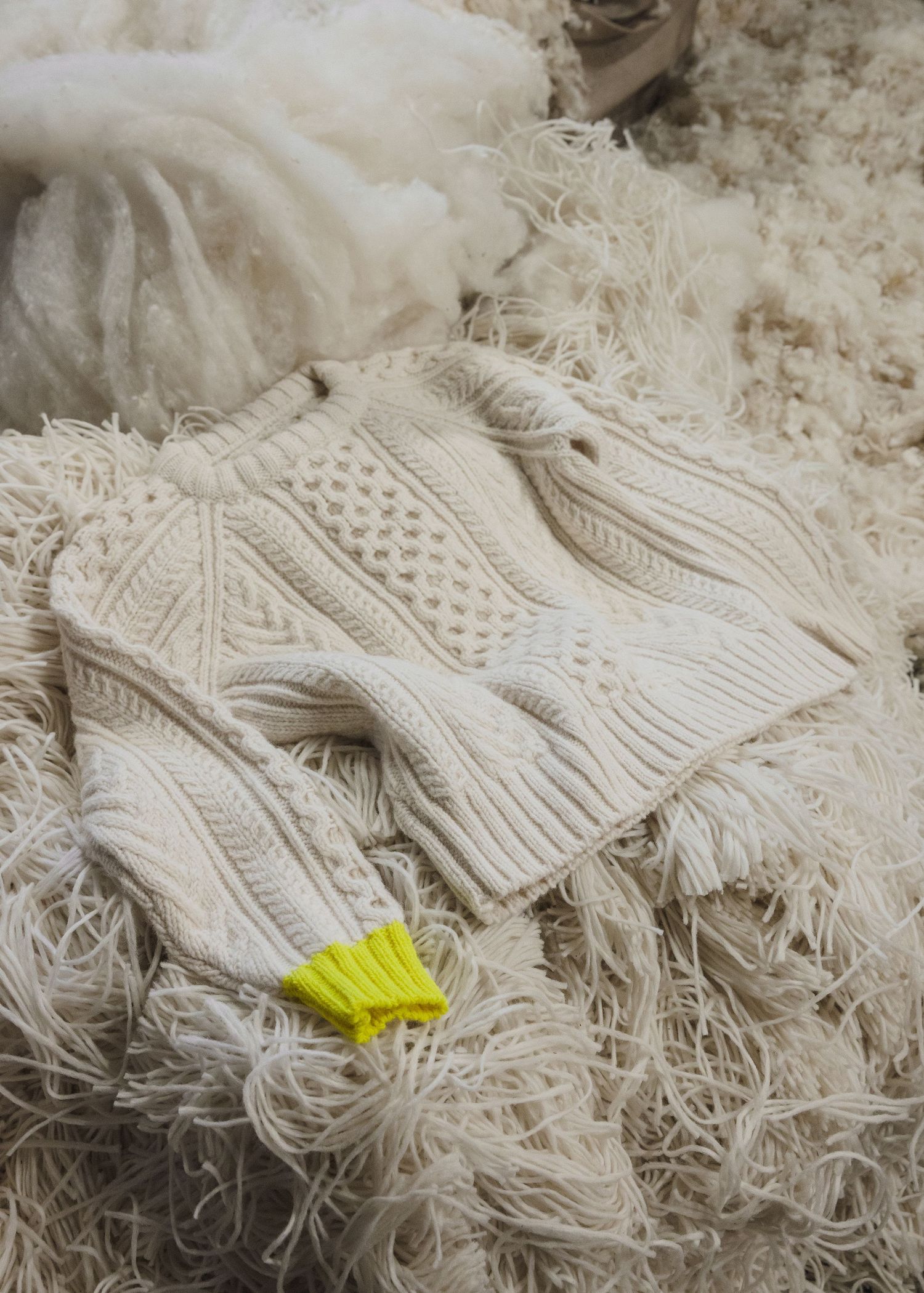A bright yellow butterfly rests on a cream-colored knit sweater with intricate cable patterns against a textured background.