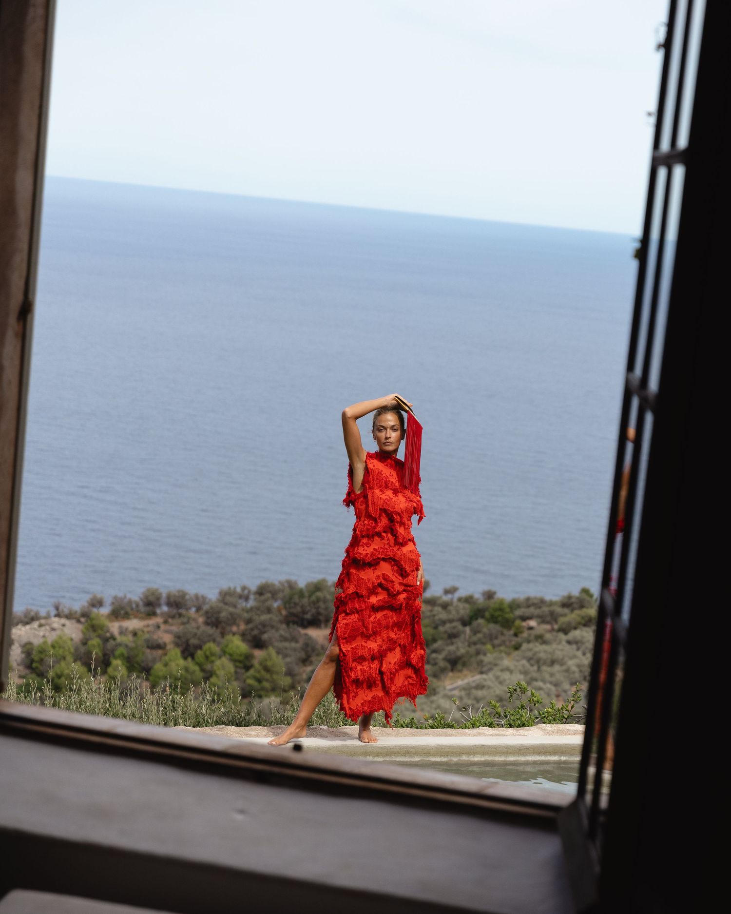 Campaign Photography. A red dress moves across multiple window frames with an ocean view backdrop, creating a dynamic visual sequence.