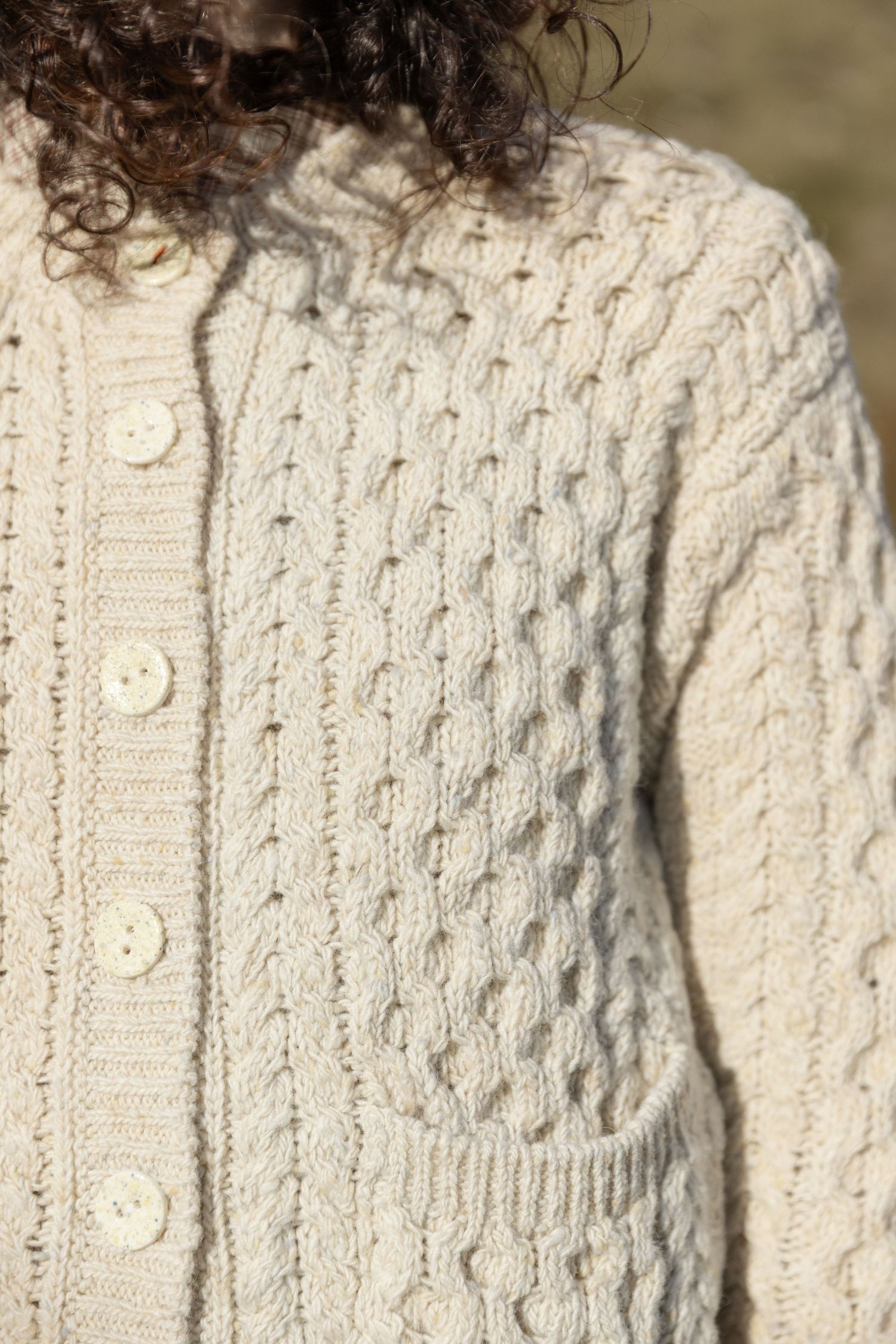 Close-up detail of a white cable knit sweater showing intricate braided pattern and textured stitching.