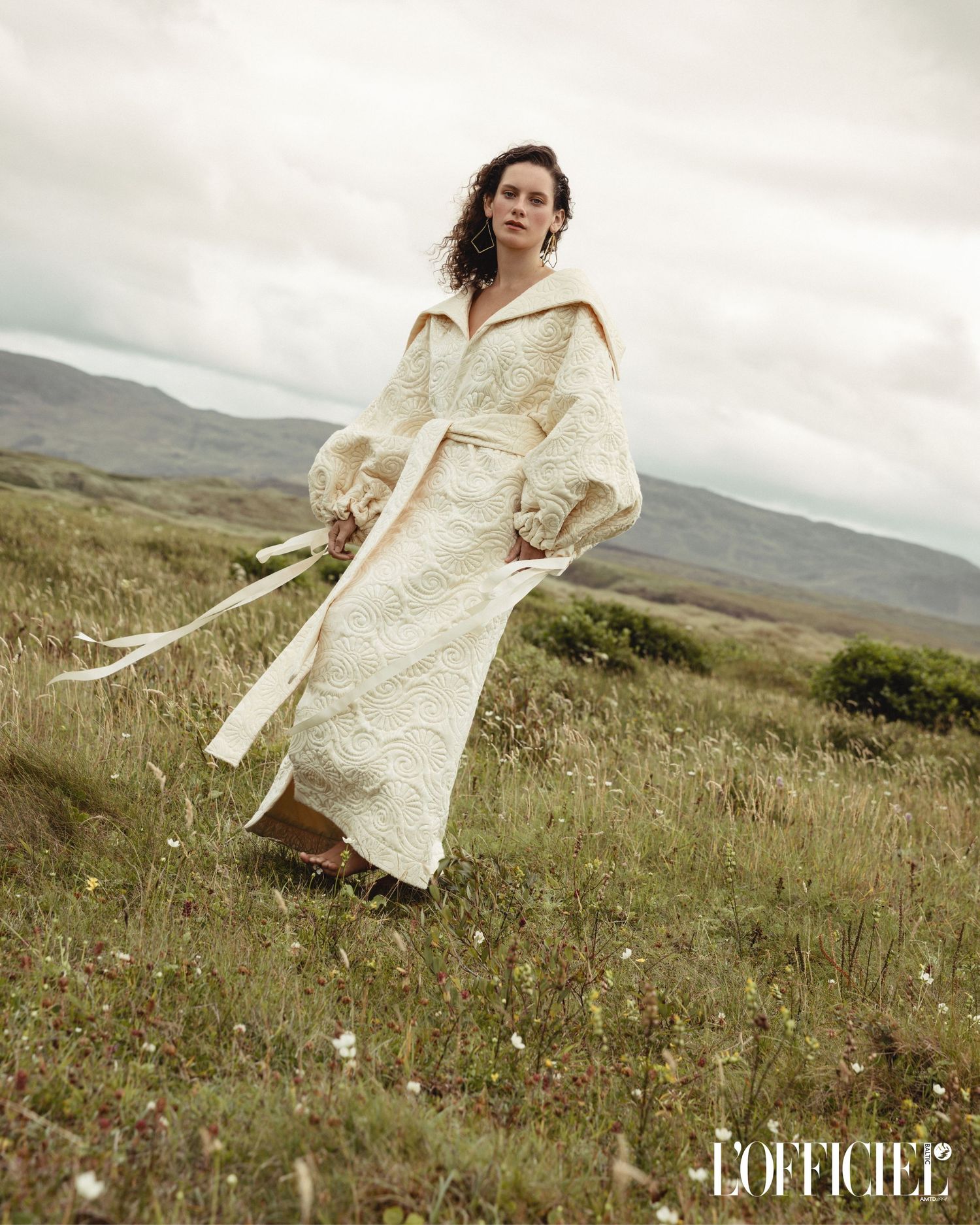 Model wearing cream-coloured coat poses in misty highland meadow landscape, editorial shoot in Donegal, Ireland rustic remote location.