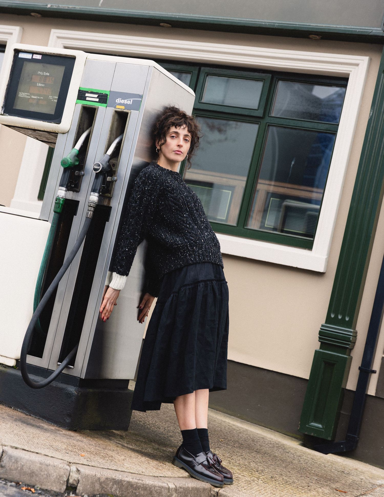 A series of fashion photos showing a black dress styled with chunky boots against a light building exterior, campaign shoot in rural town.