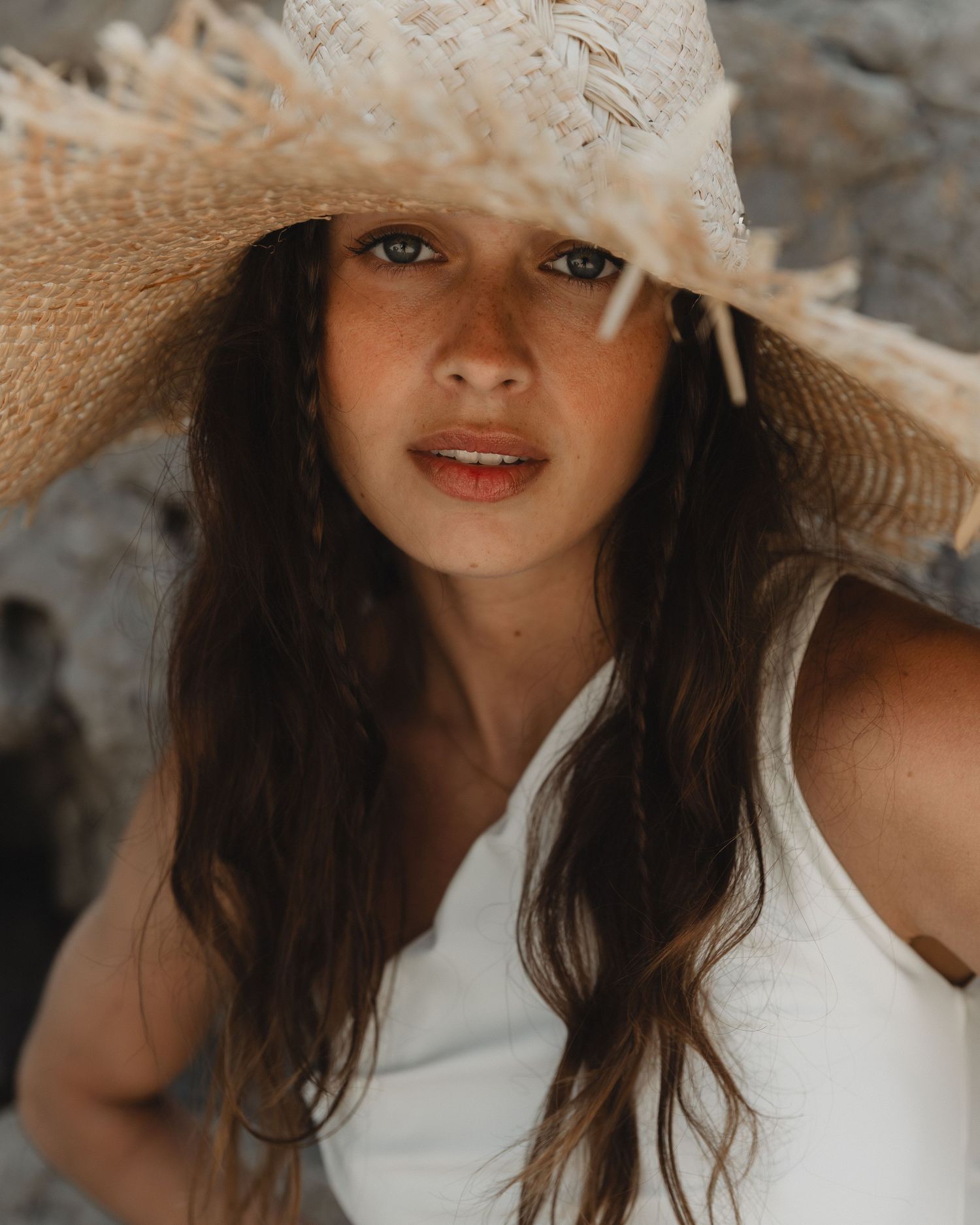 Portrait of someone wearing a large straw sun hat and white tank top in warm summer lighting.