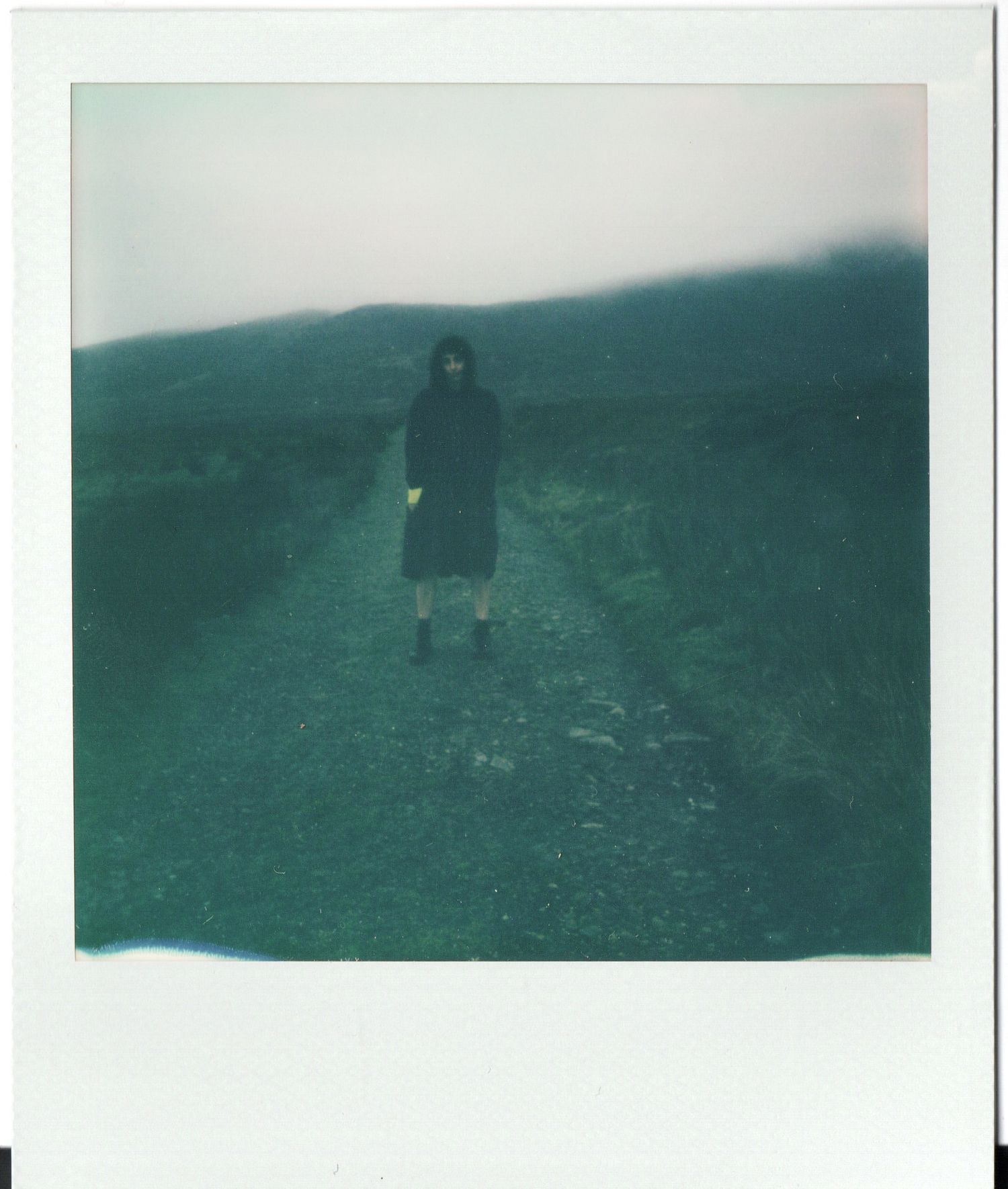A figure stands silhouetted against misty green hills in a series of vintage-style polaroid photographs.