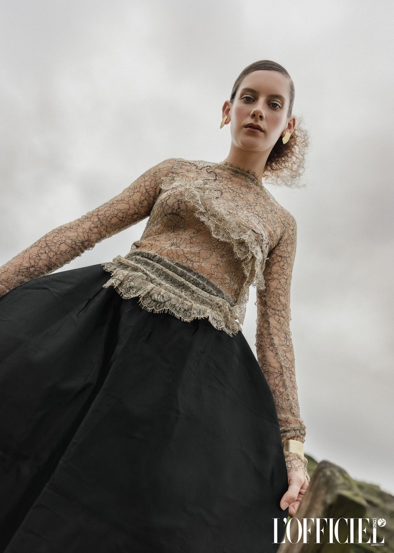 Editorial fashion series featuring elegant lace and black dress ensemble against cloudy sky published with L'Officiel.