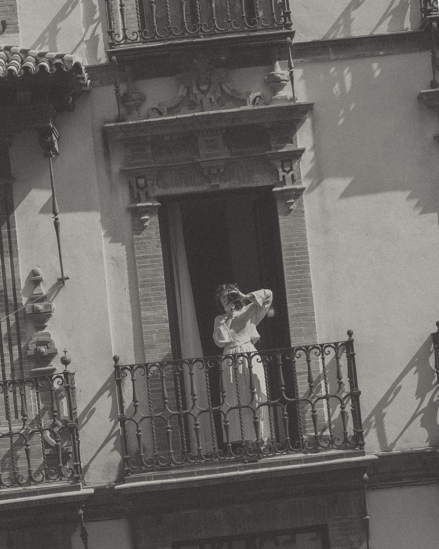 A black and white photograph shows several ornate balconies on a historic building facade casting dramatic shadows.