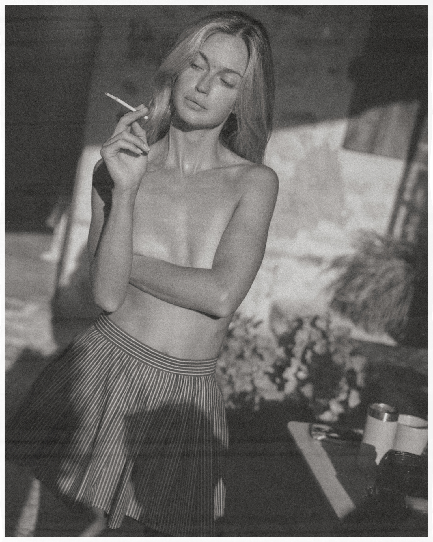 Black and white photo of a young woman in a striped skirt holding a cigarette outdoors.