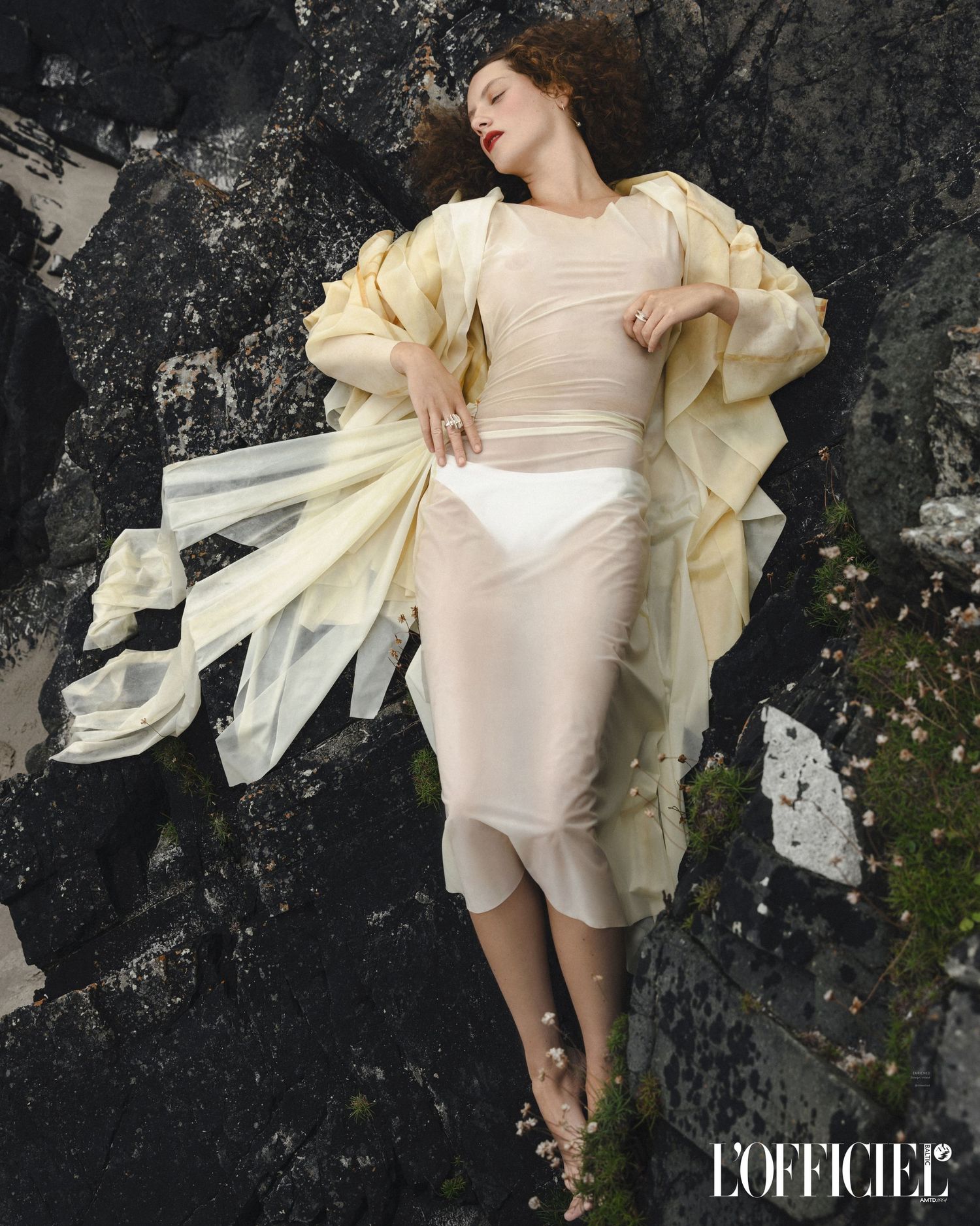 Fashion model in cream dress with dramatic ruffled sleeves poses against textured dark wall for L'Officiel magazine.