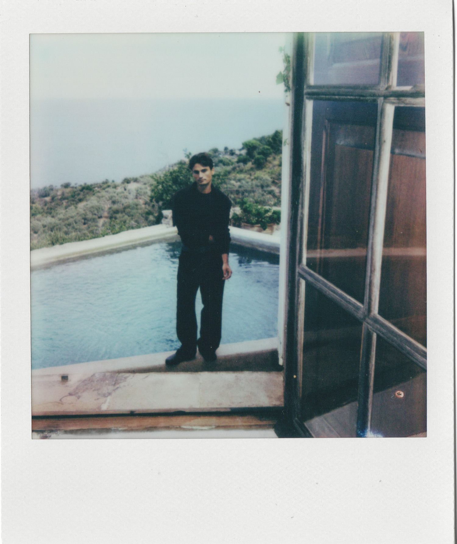 Person in dark attire stands on balcony overlooking coastal waters in vintage polaroid style photos.
