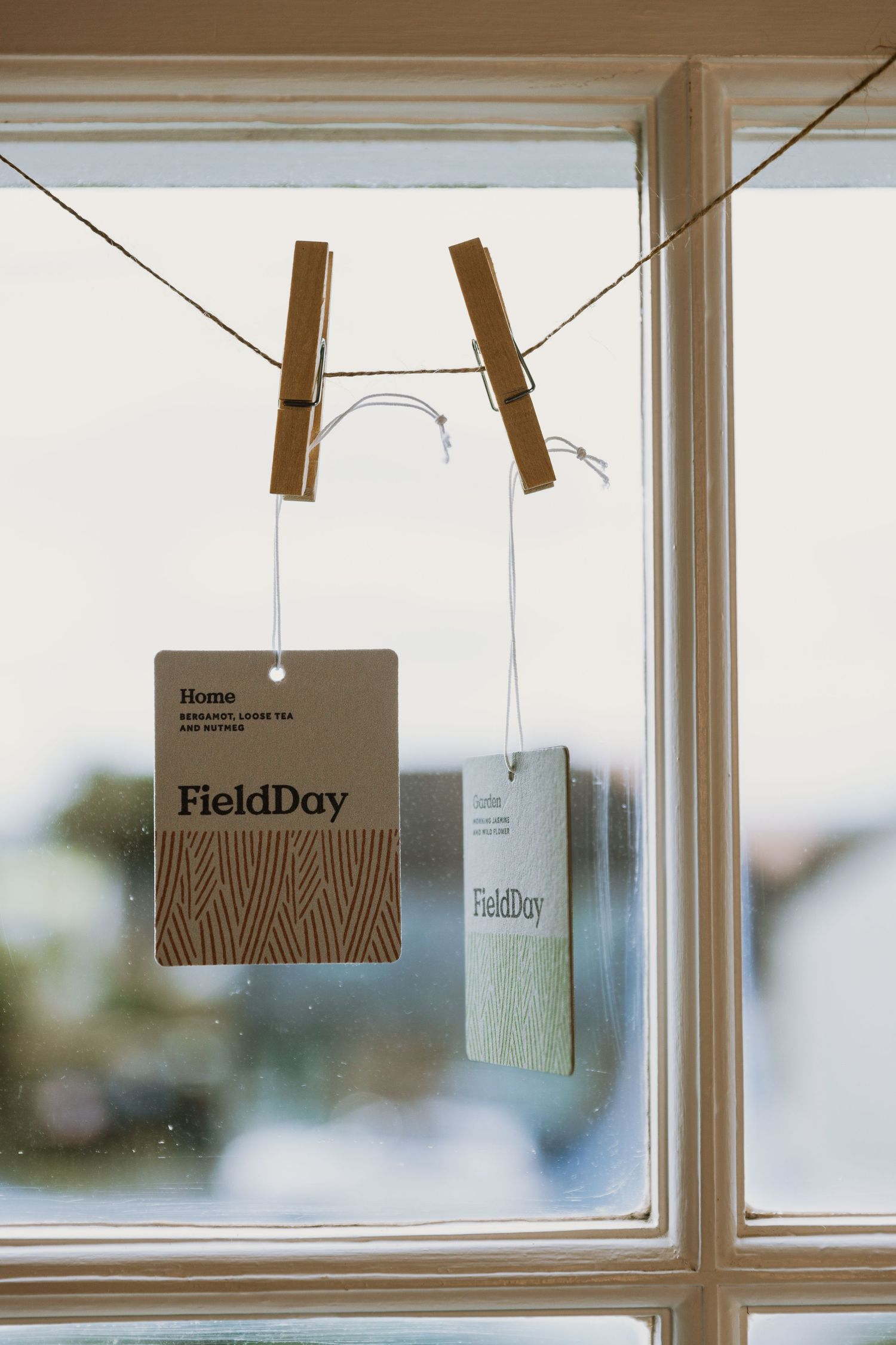 Brown paper tags with minimalist branding hang from strings against a bright window backdrop.