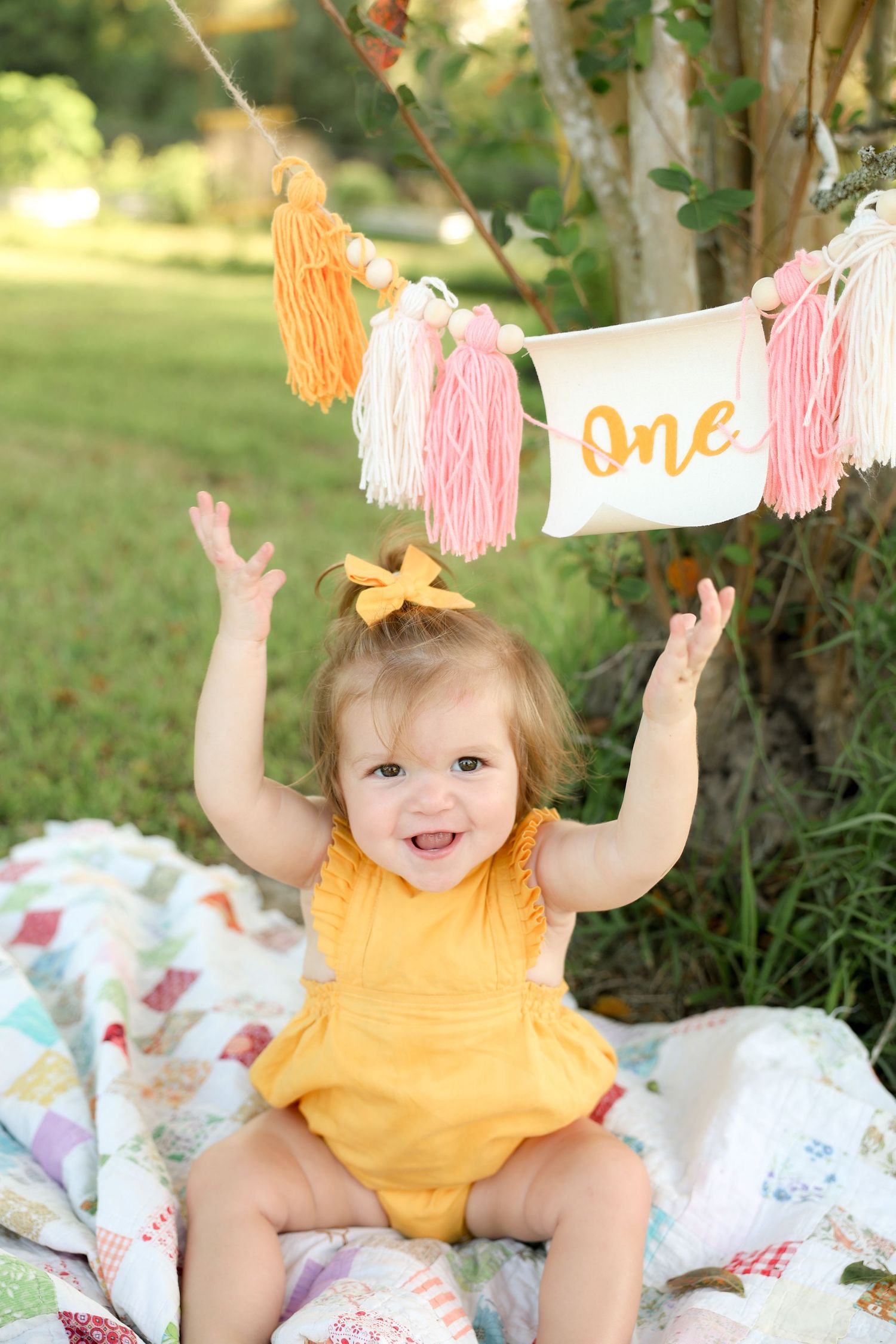 first birthday photos one year old girl in yellow dress with arms raised and one birthday sign alvin texas outdoor photography
