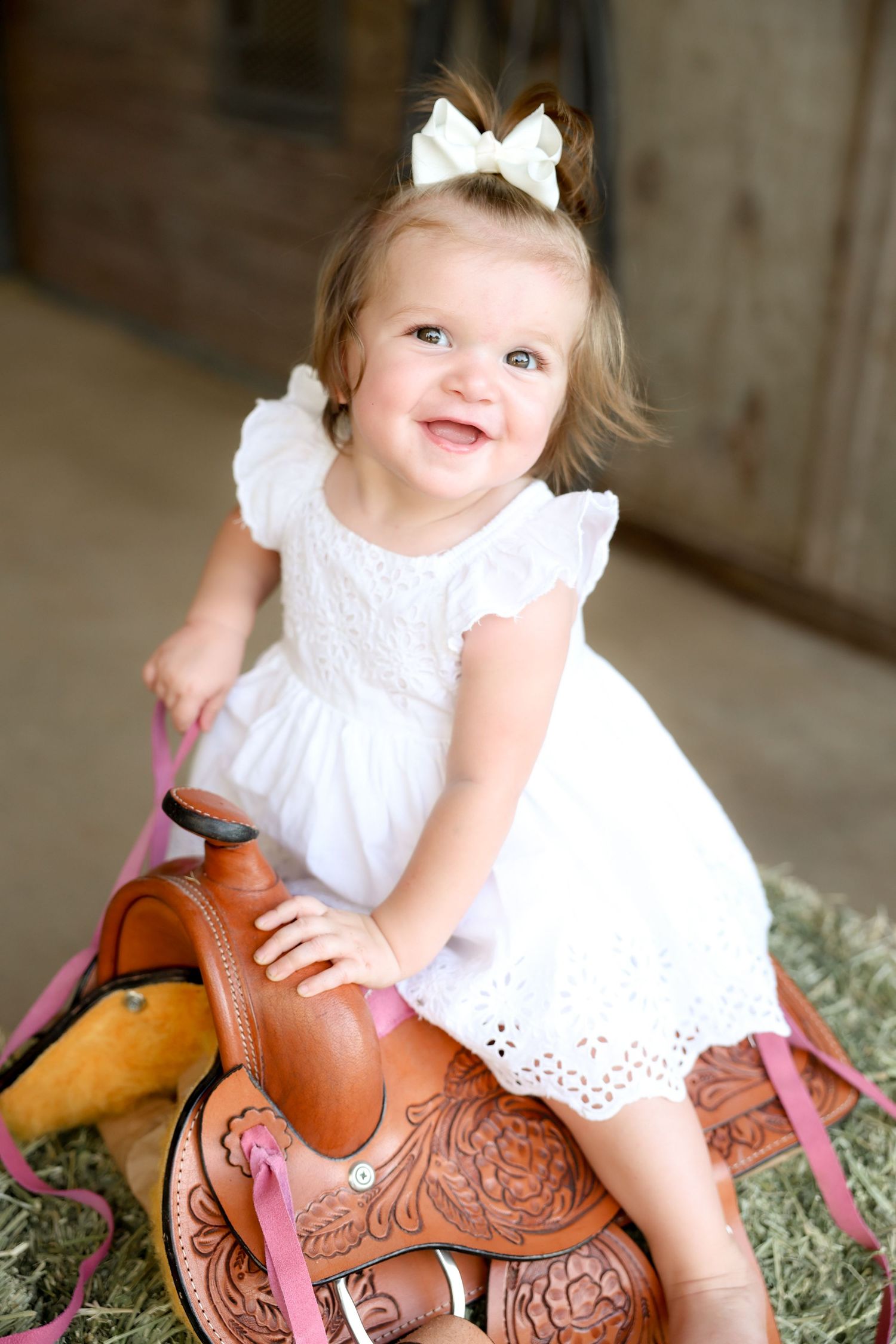 one year old photo girl on pink saddle with white dress and bow