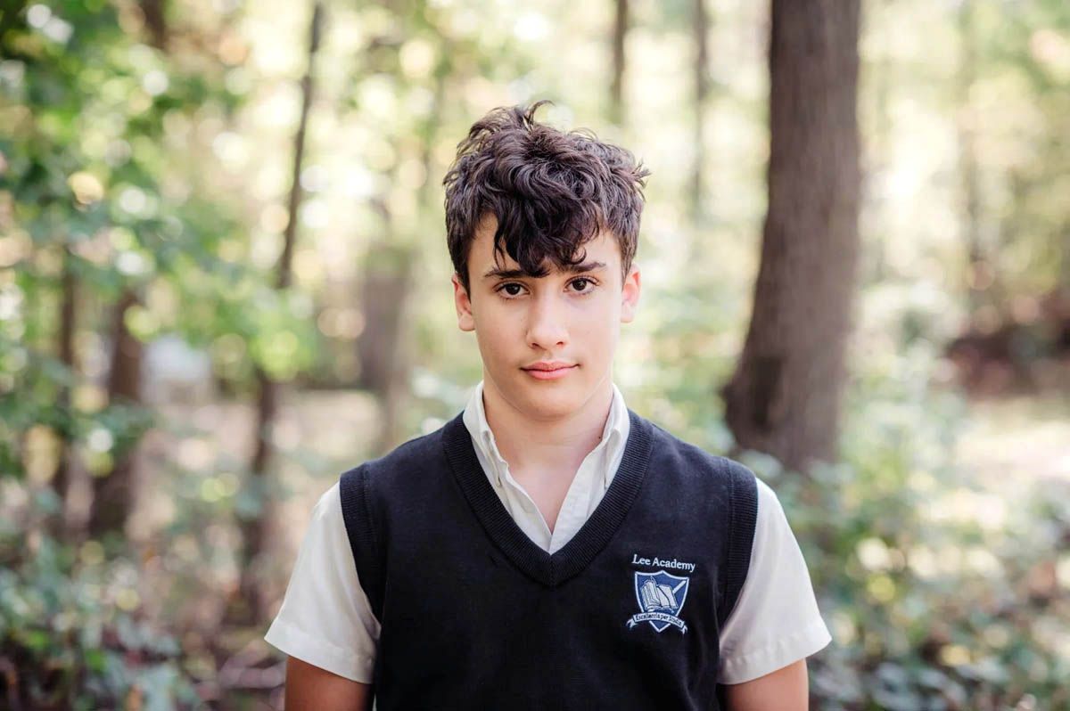 Student in school uniform stands against natural woodland background.