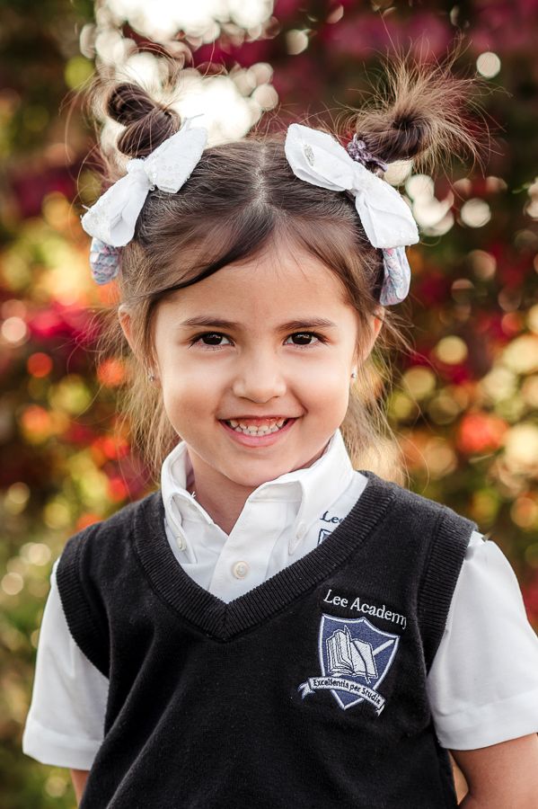 Young student in school uniform smiling brightly against colorful autumn background.