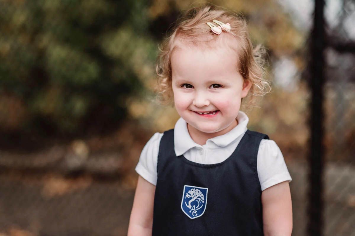 Young students wearing white collared shirts and navy vests smile during a sunny autumn photoshoot.