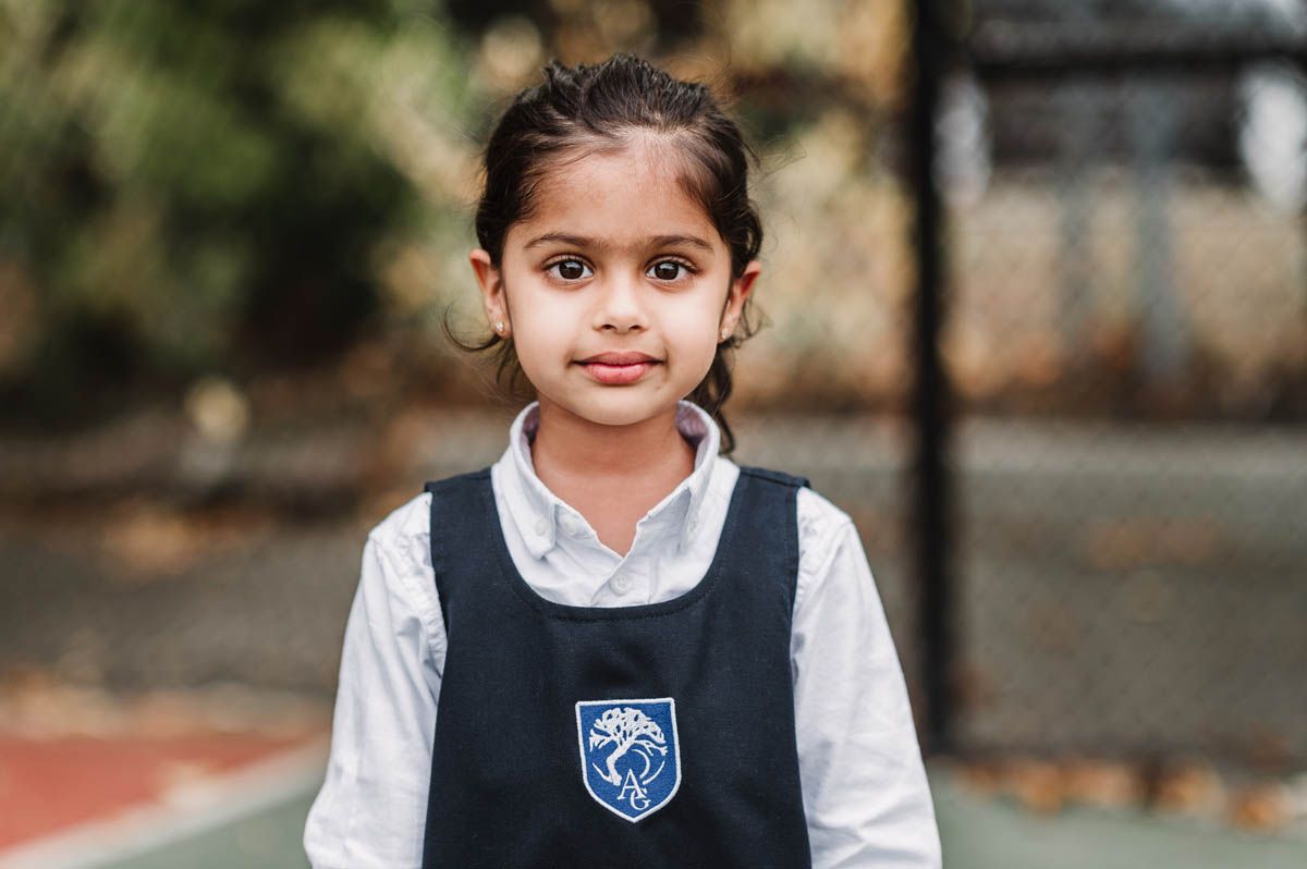 Student wearing navy blue vest uniform and white shirt poses outdoors.