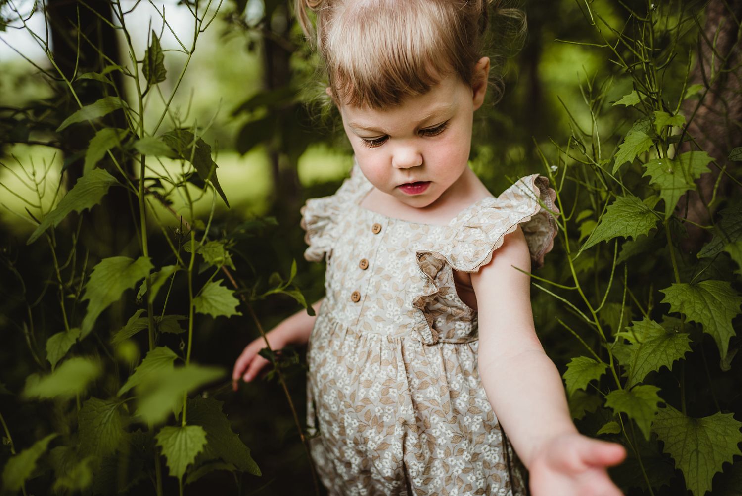 Child exploring among lush green foliage in a garden setting.