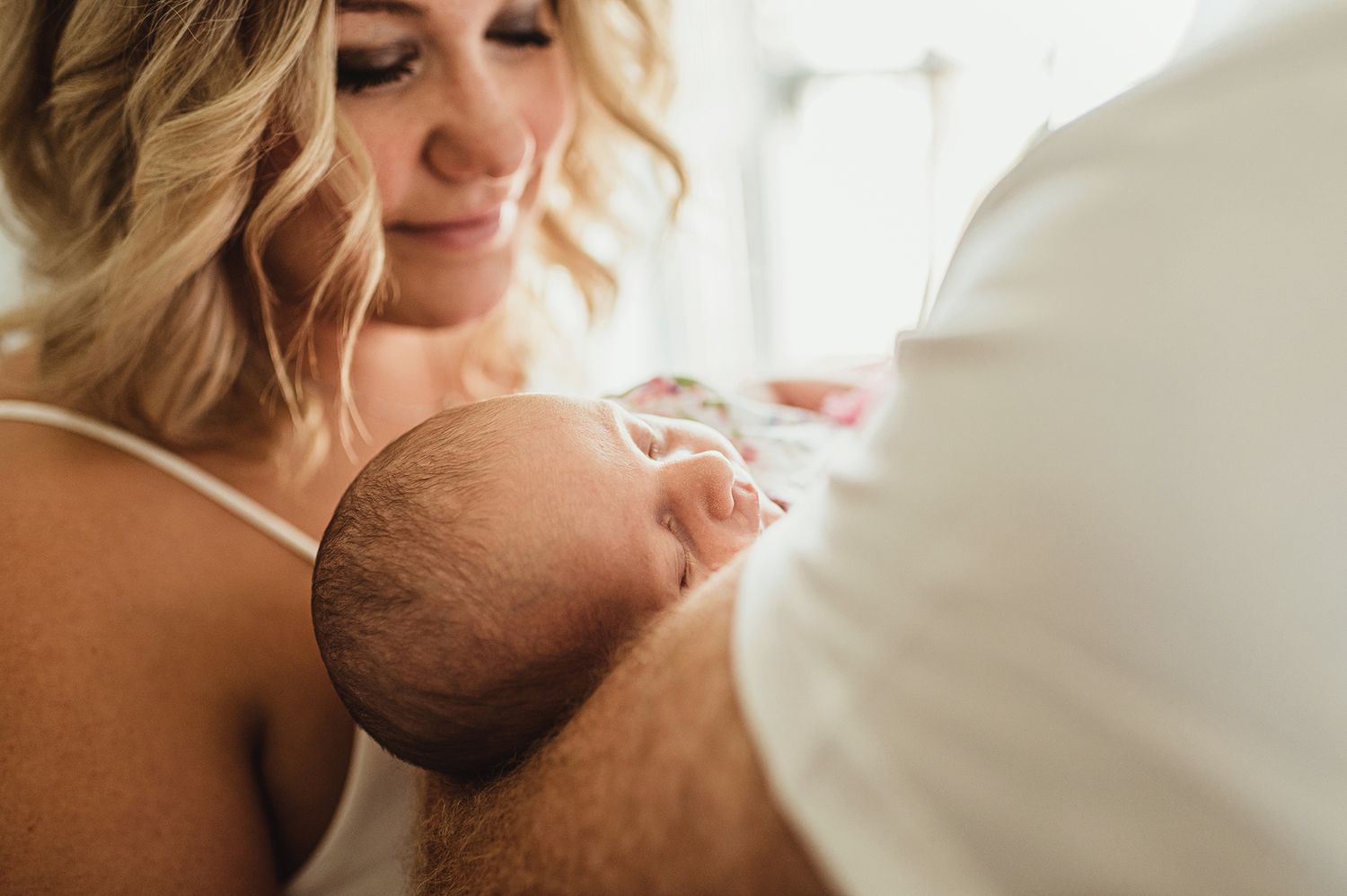 Tender moment between parent and newborn baby in soft natural light.