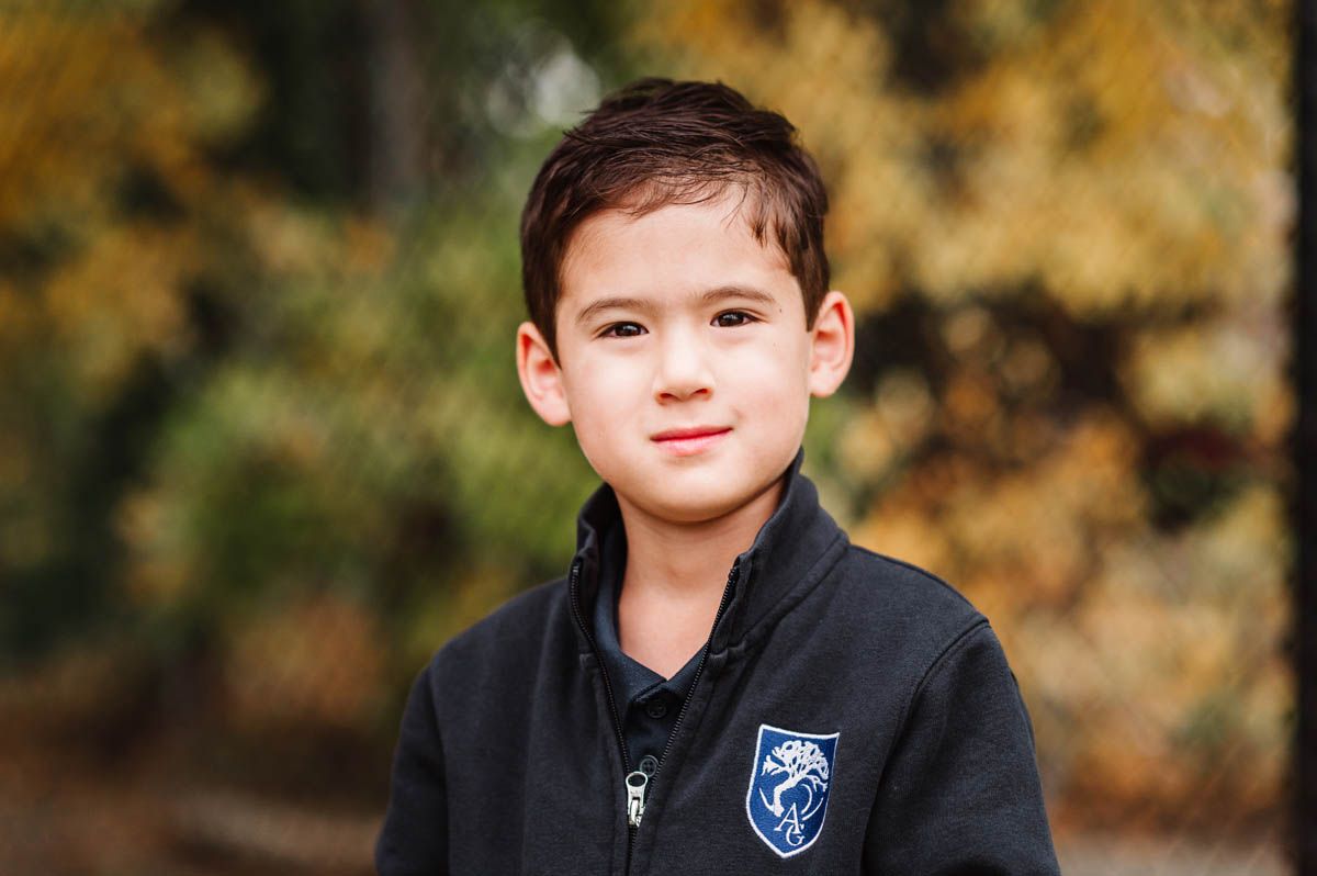 Student in navy school uniform vest poses for portrait against autumn foliage background.
