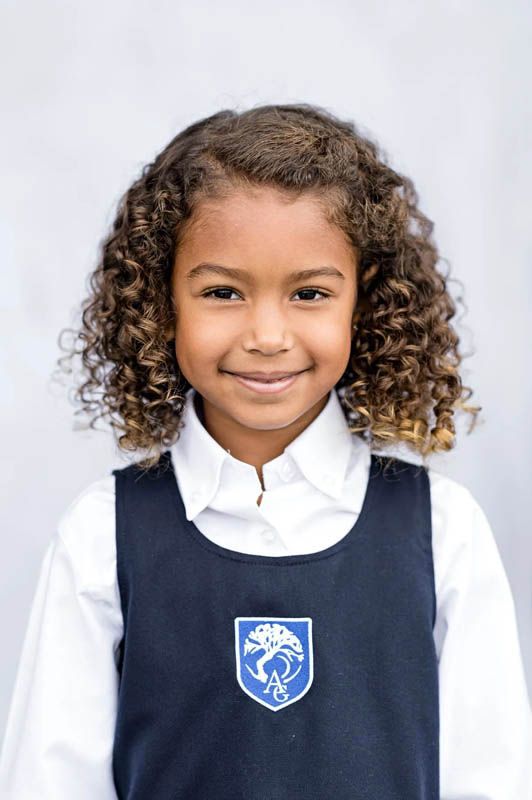 Student in navy blue vest uniform with school crest poses against white background for portraits.