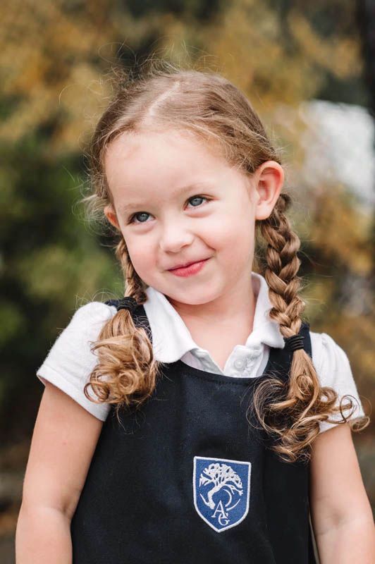 Young student in school uniform with braided hair poses for portraits outdoors.